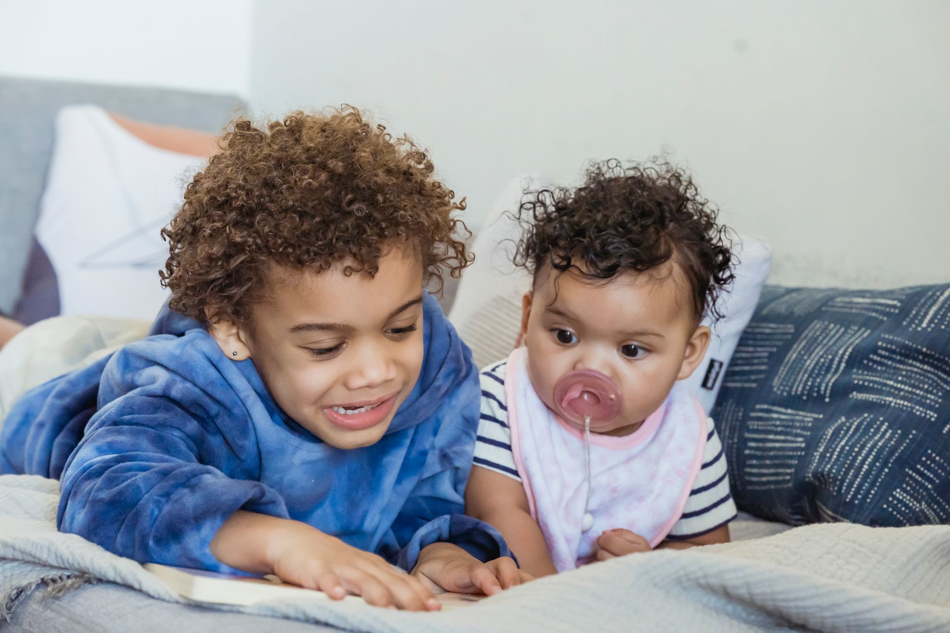 A boy and a baby are laying on a bed reading a book together.
