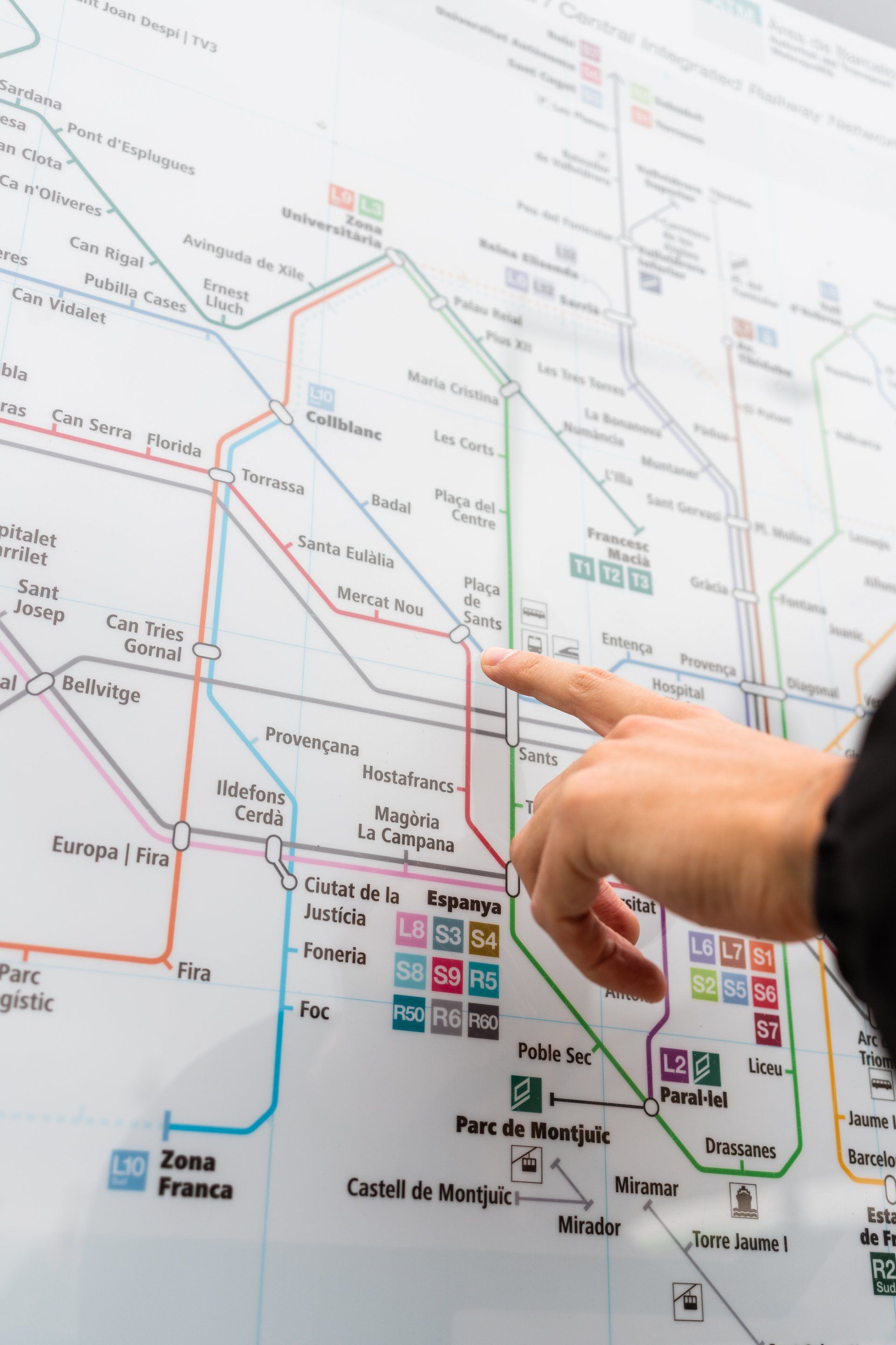 Hand pointing to a metro map, highlighting a station with colorful lines indicating routes.