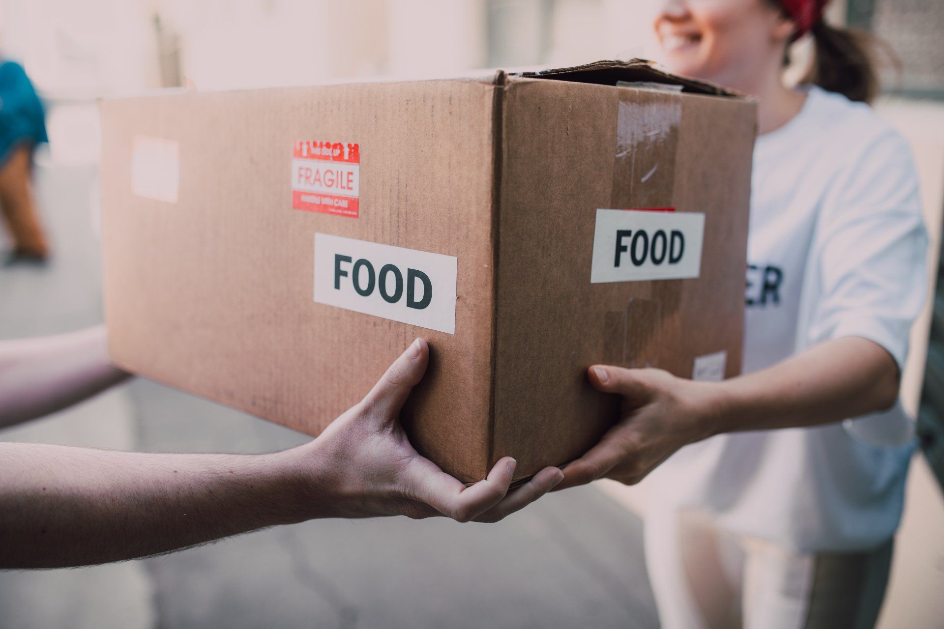 A woman is handing a box of food to another woman.