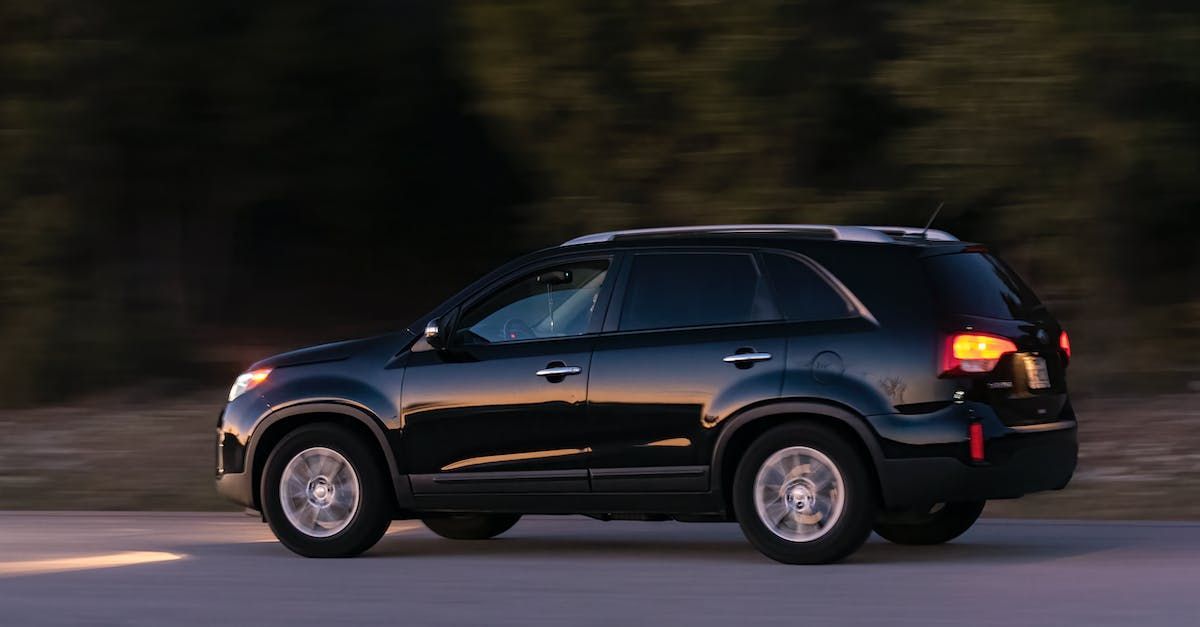 Black SUV driving on a road at dusk with blurred trees in the background