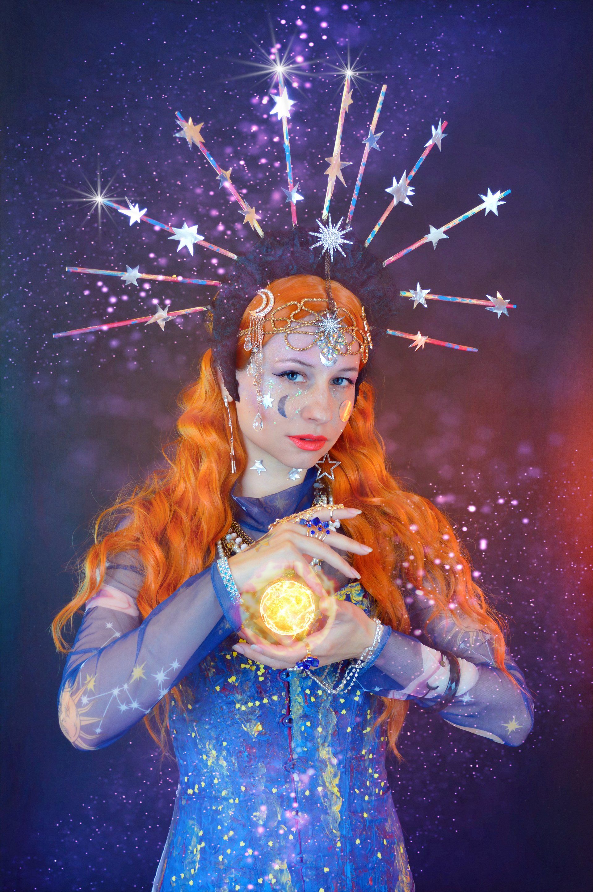 A woman with red hair and a crown on her head is holding a light in her hands.
