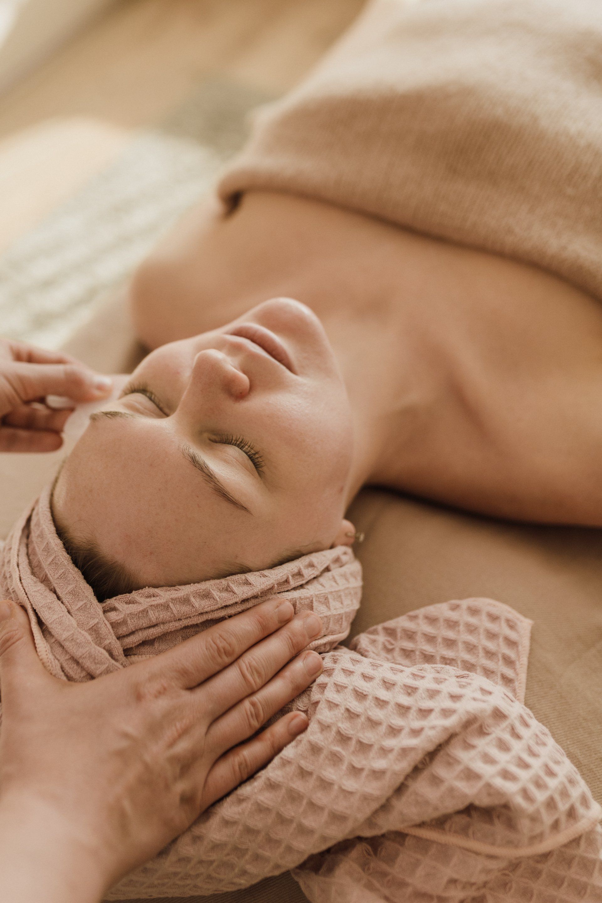 Persoon die een gezichtsmassage krijgt met een handdoek om het hoofd gewikkeld in een spa.