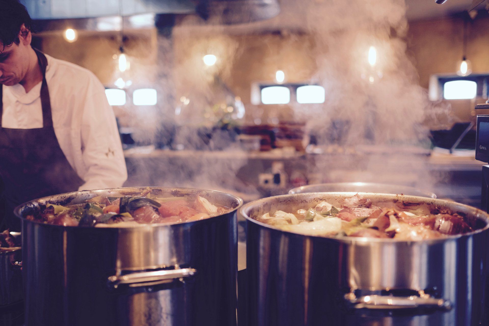 A chef is cooking food in pots in a kitchen.