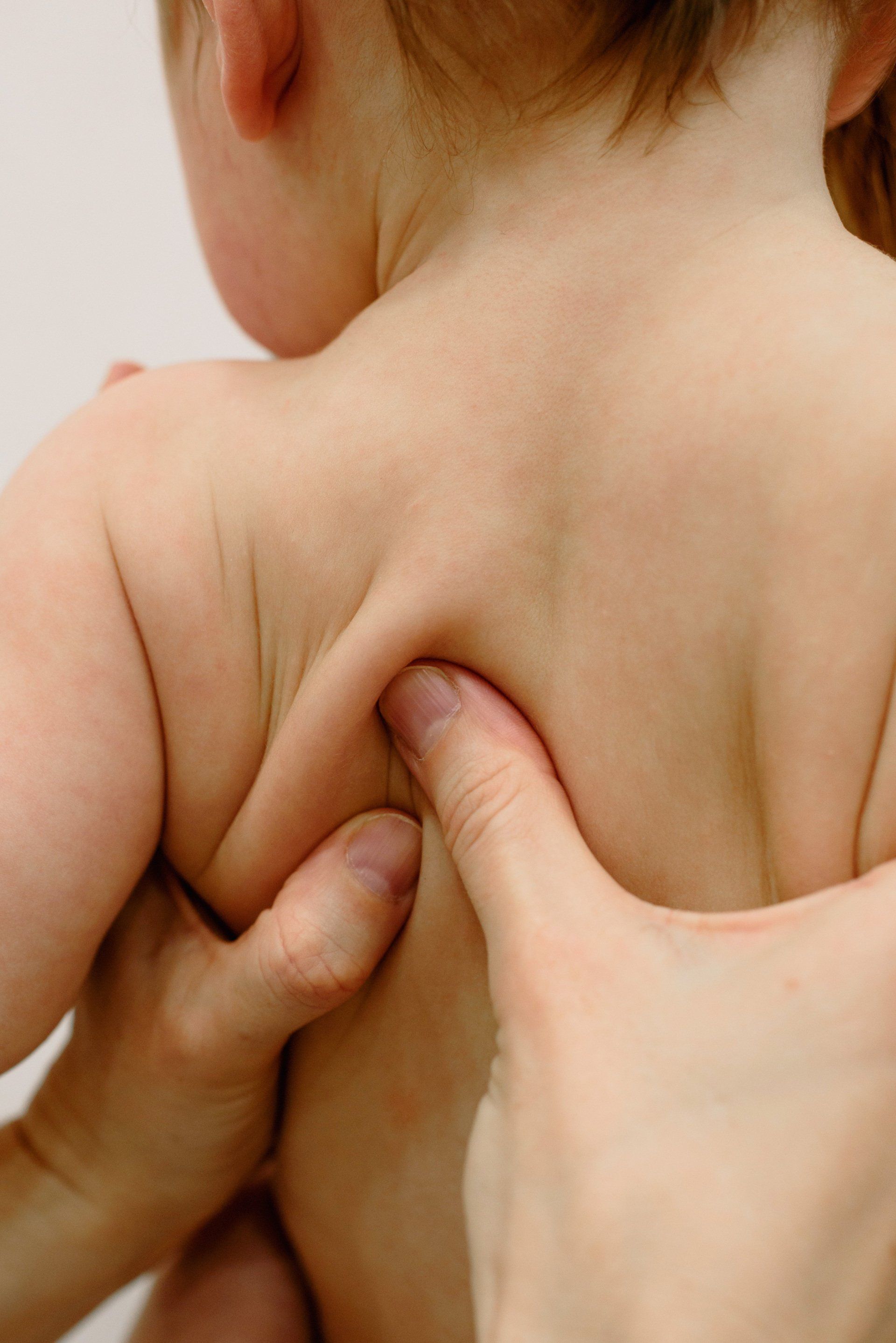 Manos de una persona masajeando la espalda de un niño pequeño, concentrándose en los omóplatos.