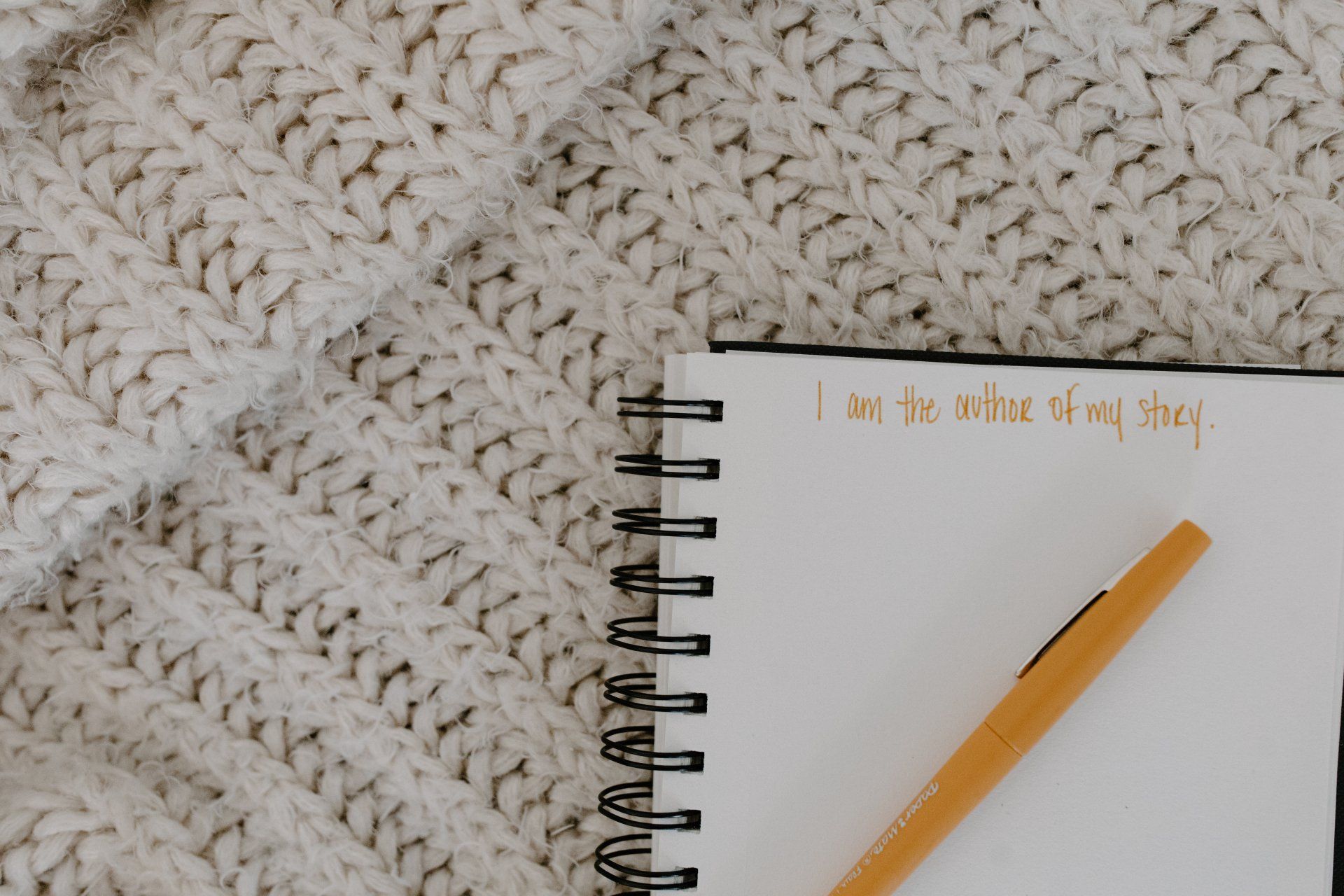 A spiral notebook and a pen are sitting on top of a knitted blanket.