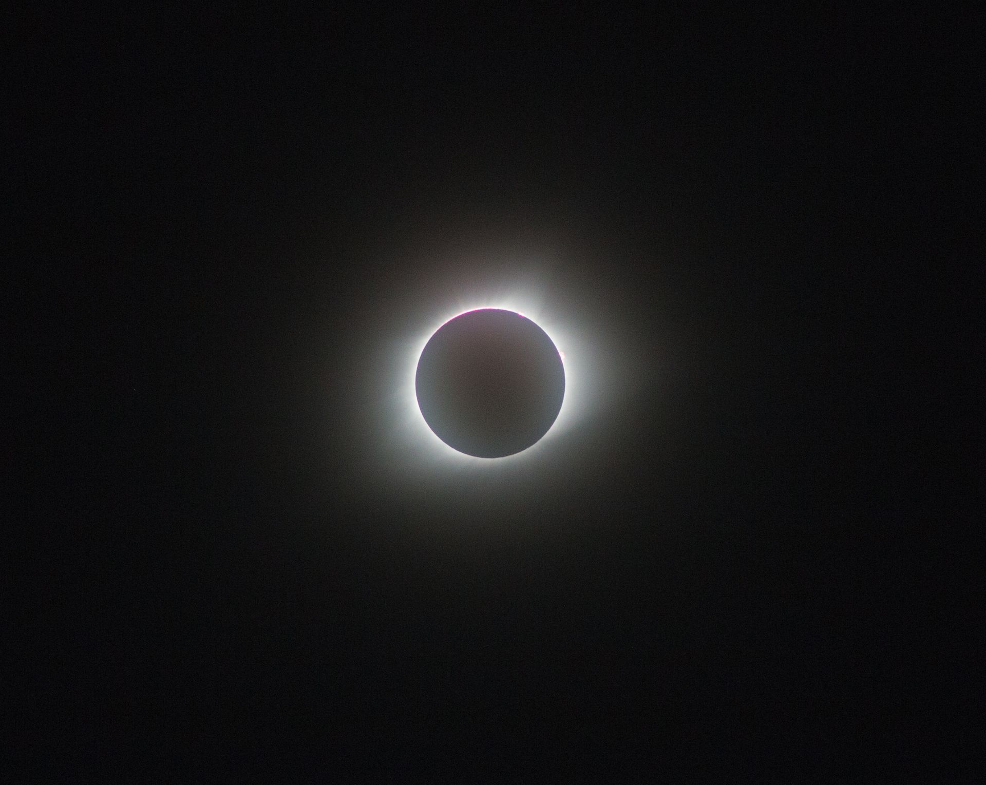A solar eclipse with a dark moon silhouetted against the glowing white corona on a black sky.