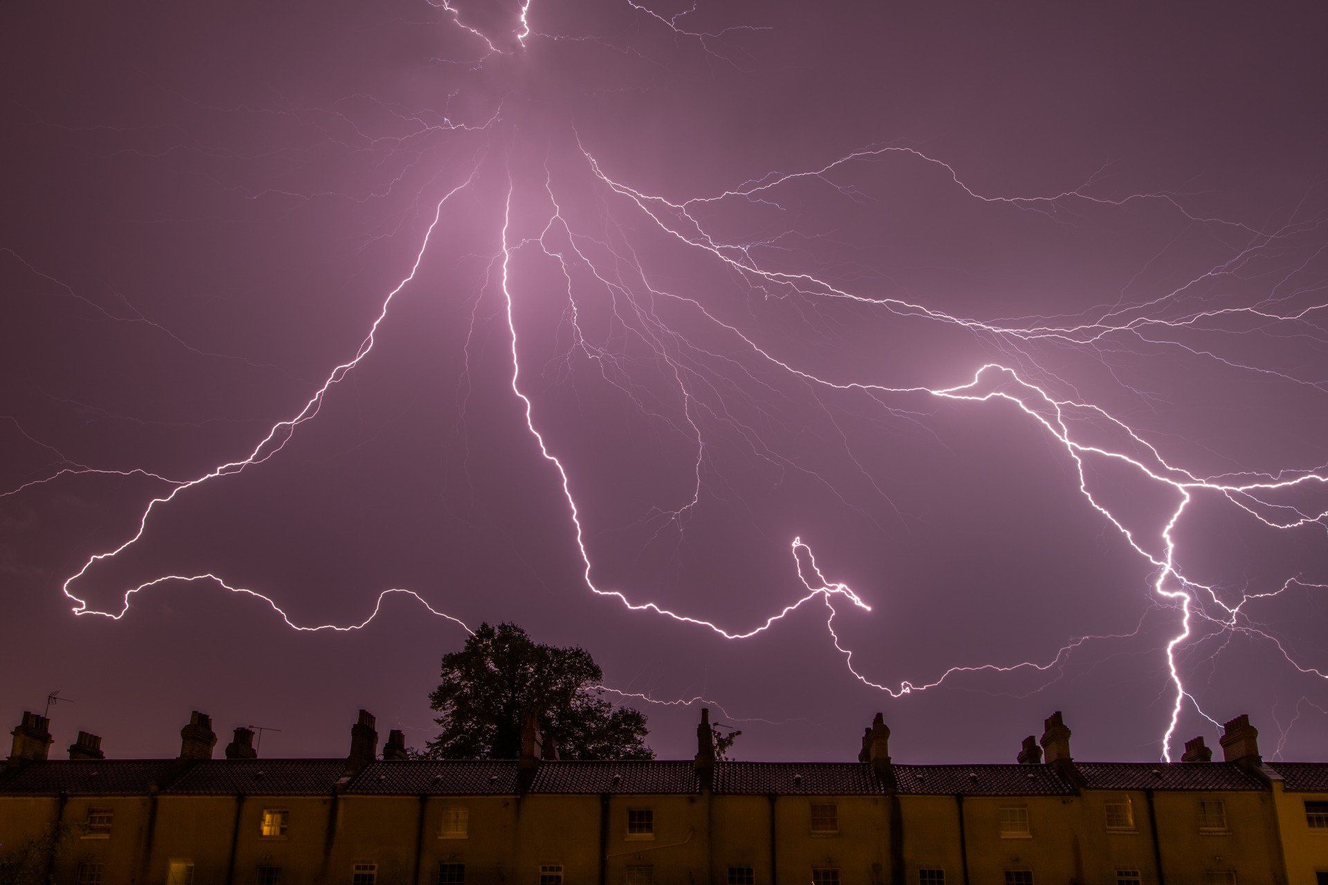 Lightning strikes over a row of houses at night.