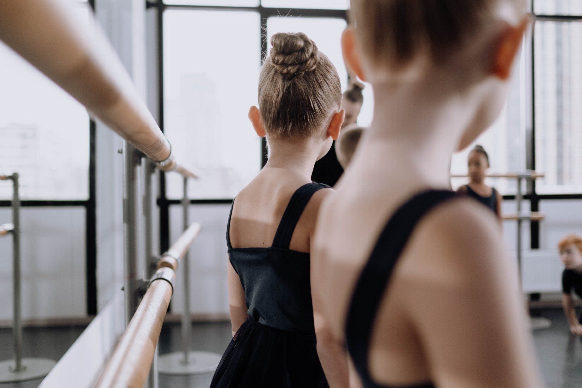 A group of young girls are standing at a ballet barre in a dance studio.
