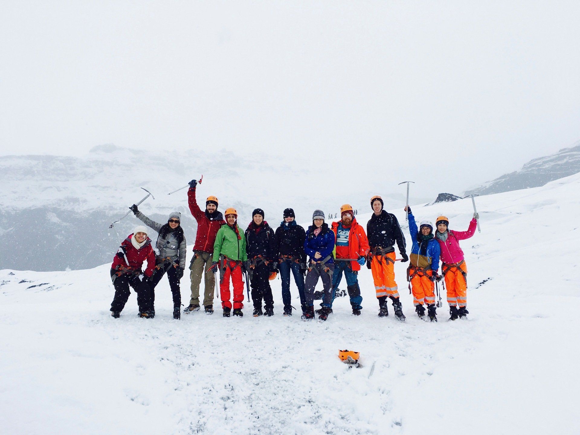 Group of people on snowy mountain, raising ice axes. Wearing helmets and colorful winter gear.