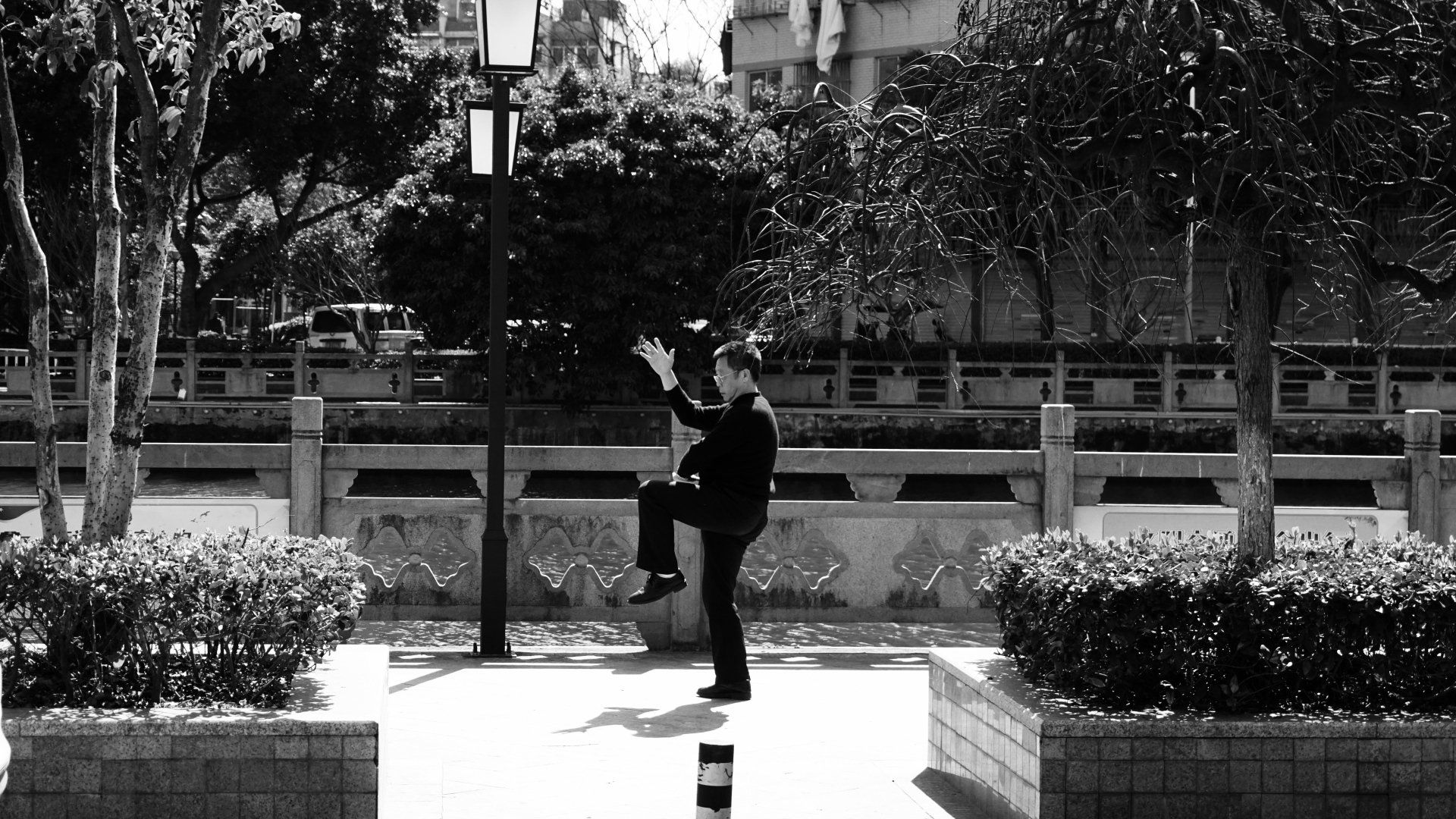 a black and white photo of a man standing on one leg doing Tai Chi