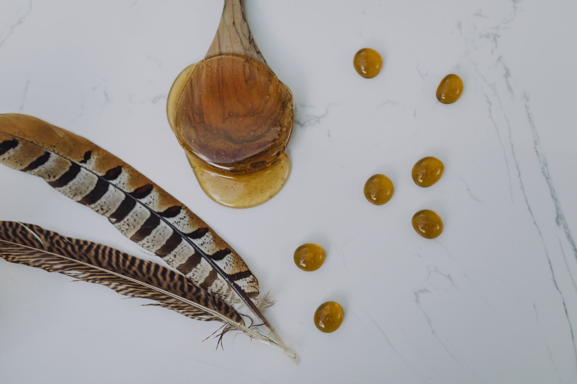 A wooden spoon filled with honey next to a feather on a white surface.