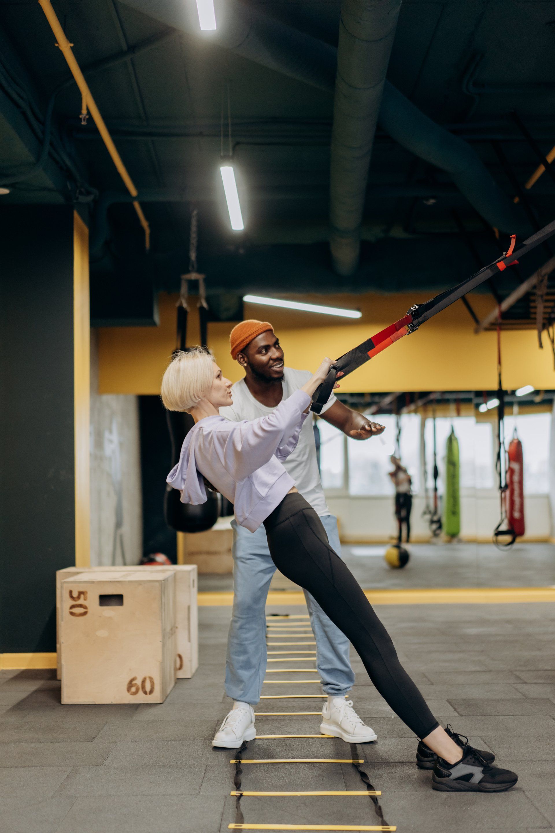 A man is helping a woman do exercises on a ladder in a gym.