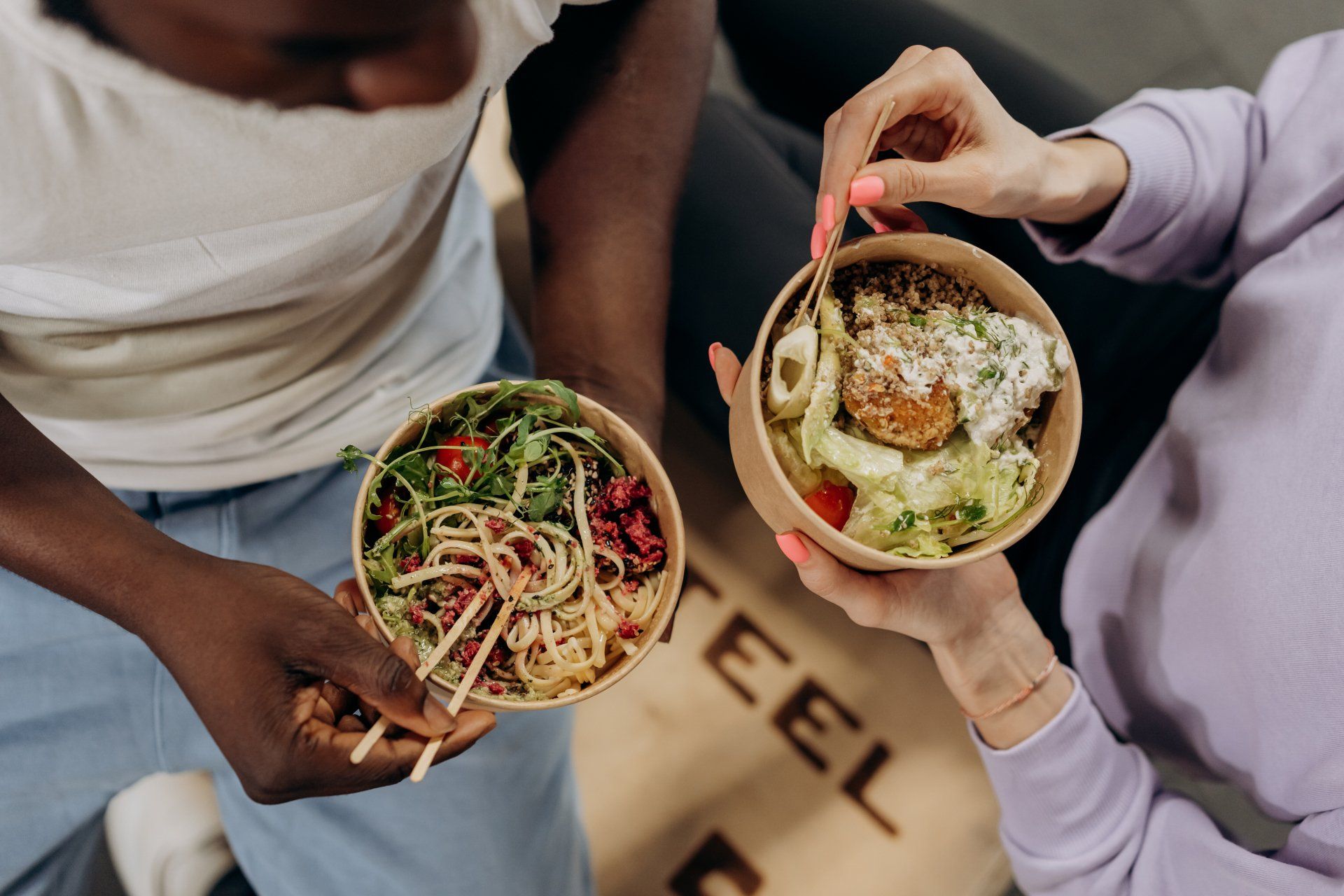 a man and a woman are holding bowls of food and eating together