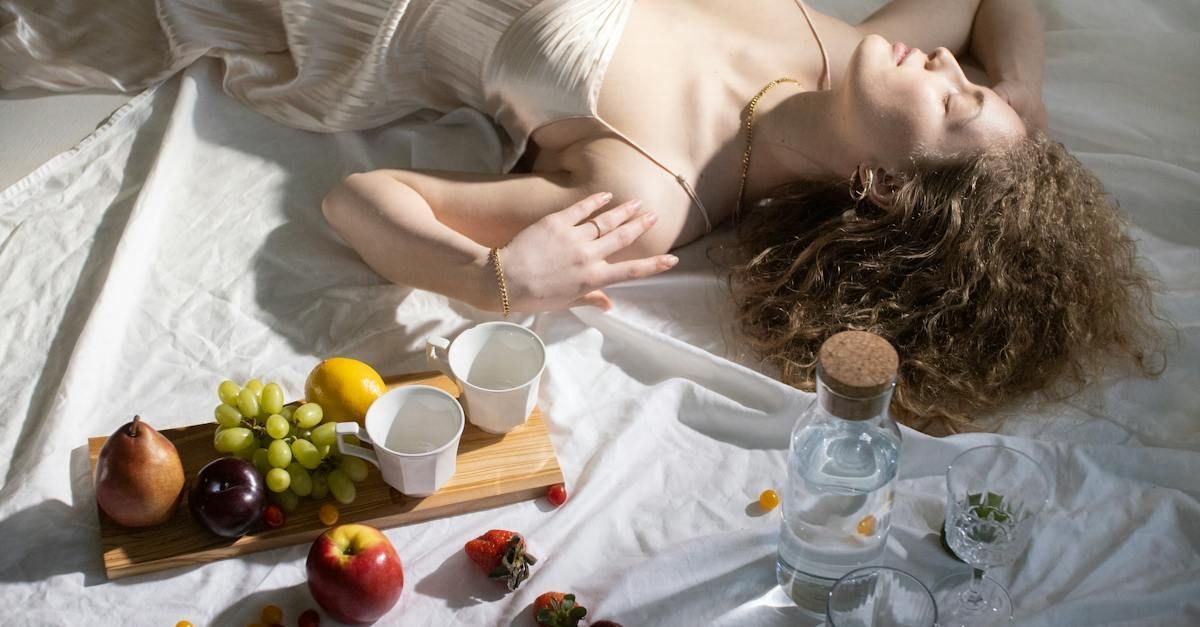 Woman relaxing with fruit and drinks. Sunlight bathes a white sheet.