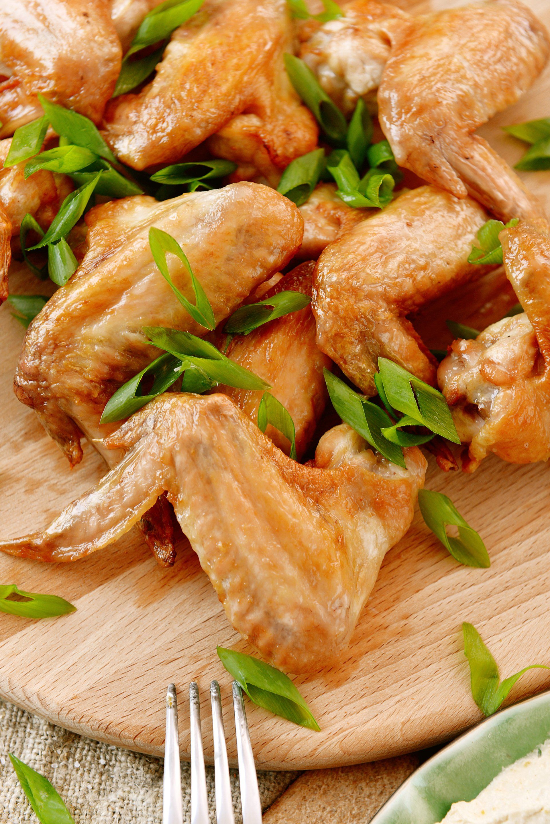 Fried chicken wings with green onion garnish on a wooden board.