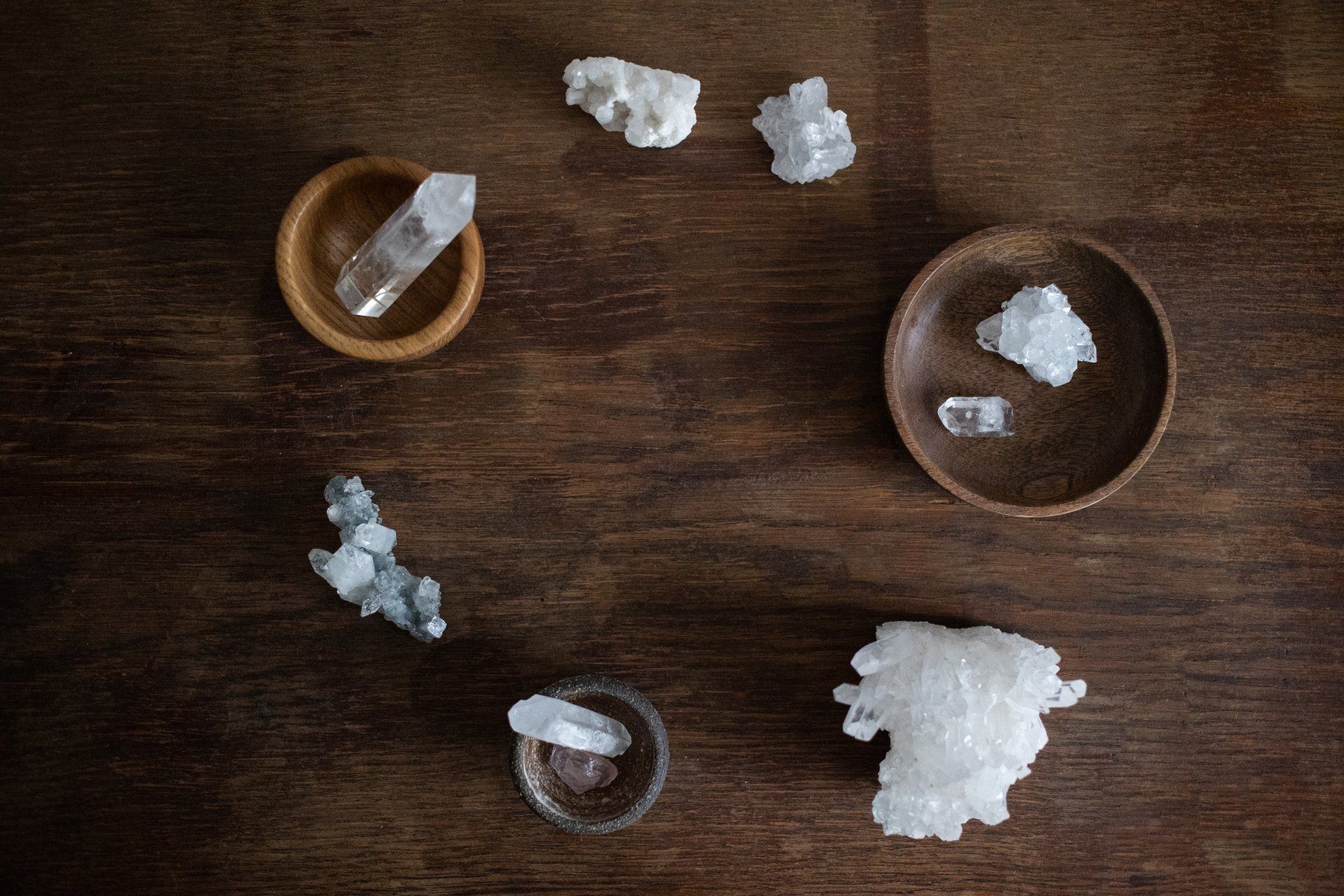 Crystals arranged in a circle on a dark wood surface; crystals in wooden bowls, various shapes and sizes.
