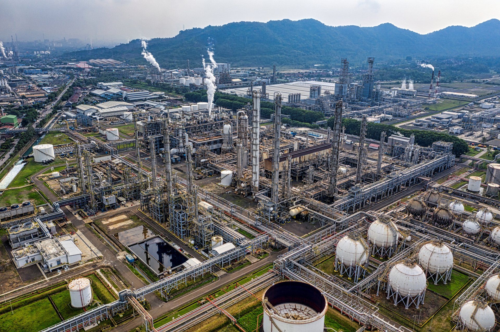 An aerial view of a large oil refinery with mountains in the background.