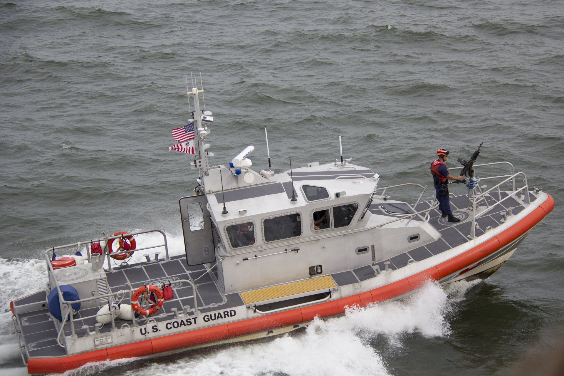 Coast Guard rescue boat speeding through rough gray water, two crew members visible on deck
