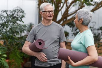 A man and a woman are holding yoga mats and talking to each other.