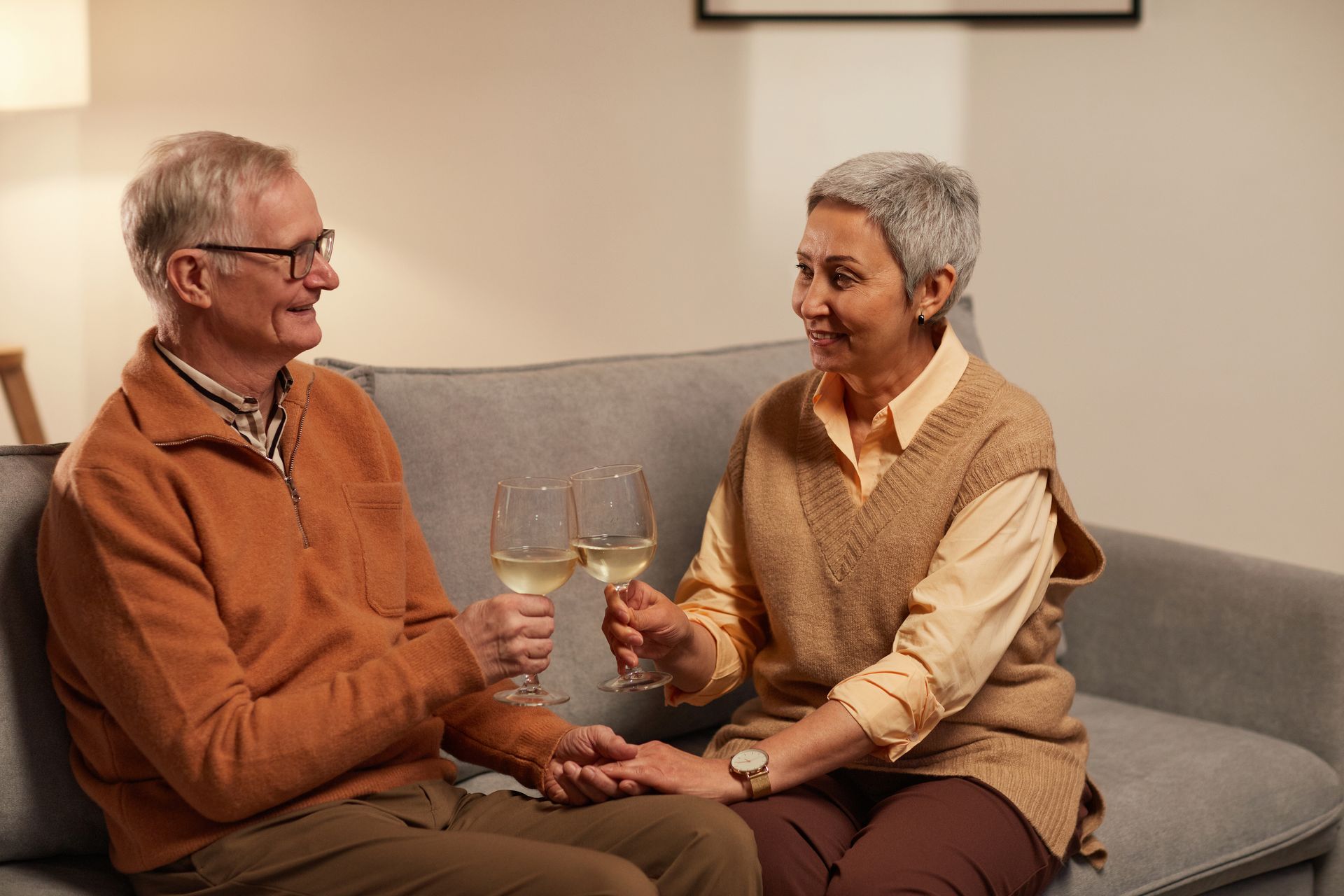 An elderly couple is sitting on a couch toasting with wine glasses.