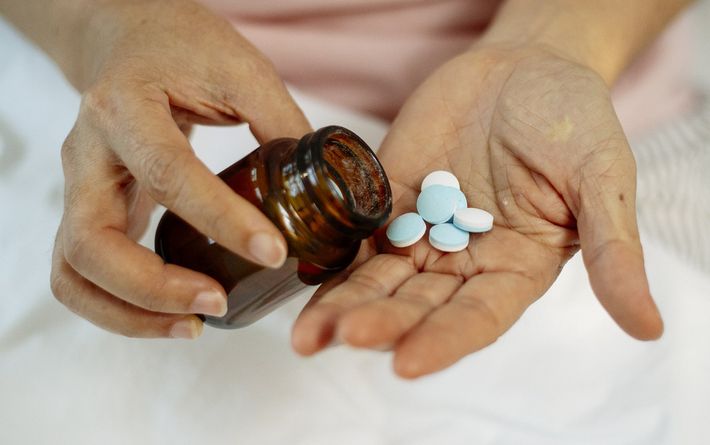 A hand pours several light blue, round pills from a brown bottle into the palm of the other hand.