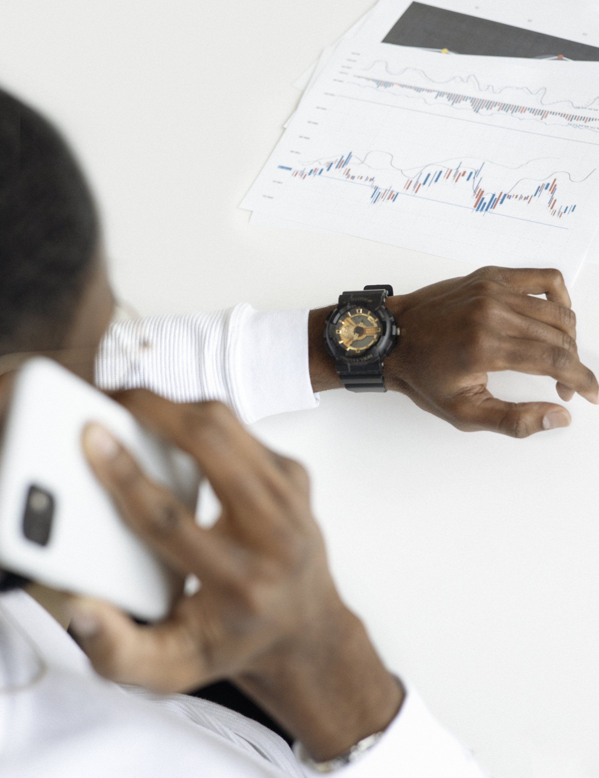 Man on phone, looking at wristwatch and financial graphs.