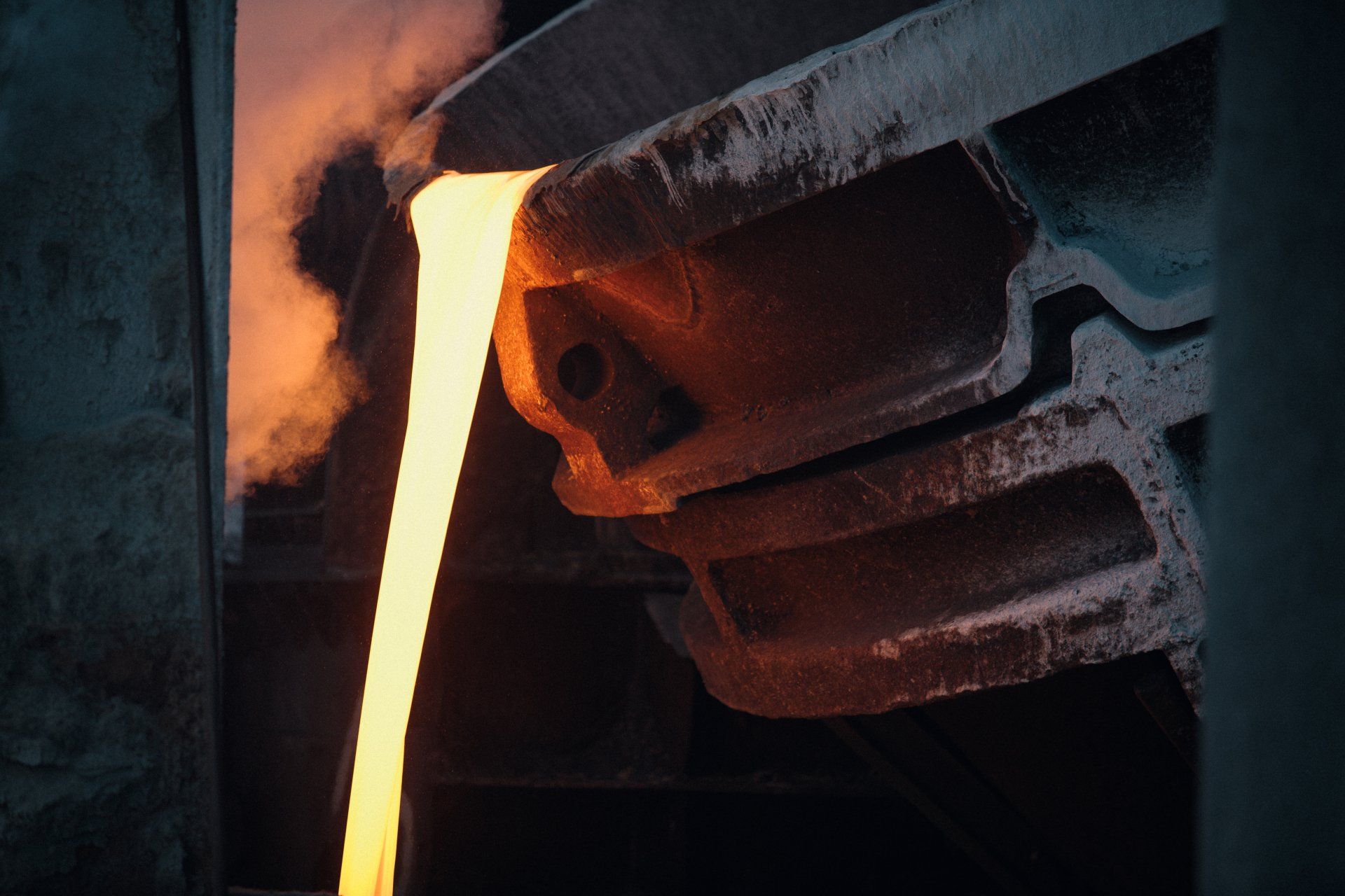 Molten metal pouring from a spout into a mold, orange and yellow hues, industrial setting.