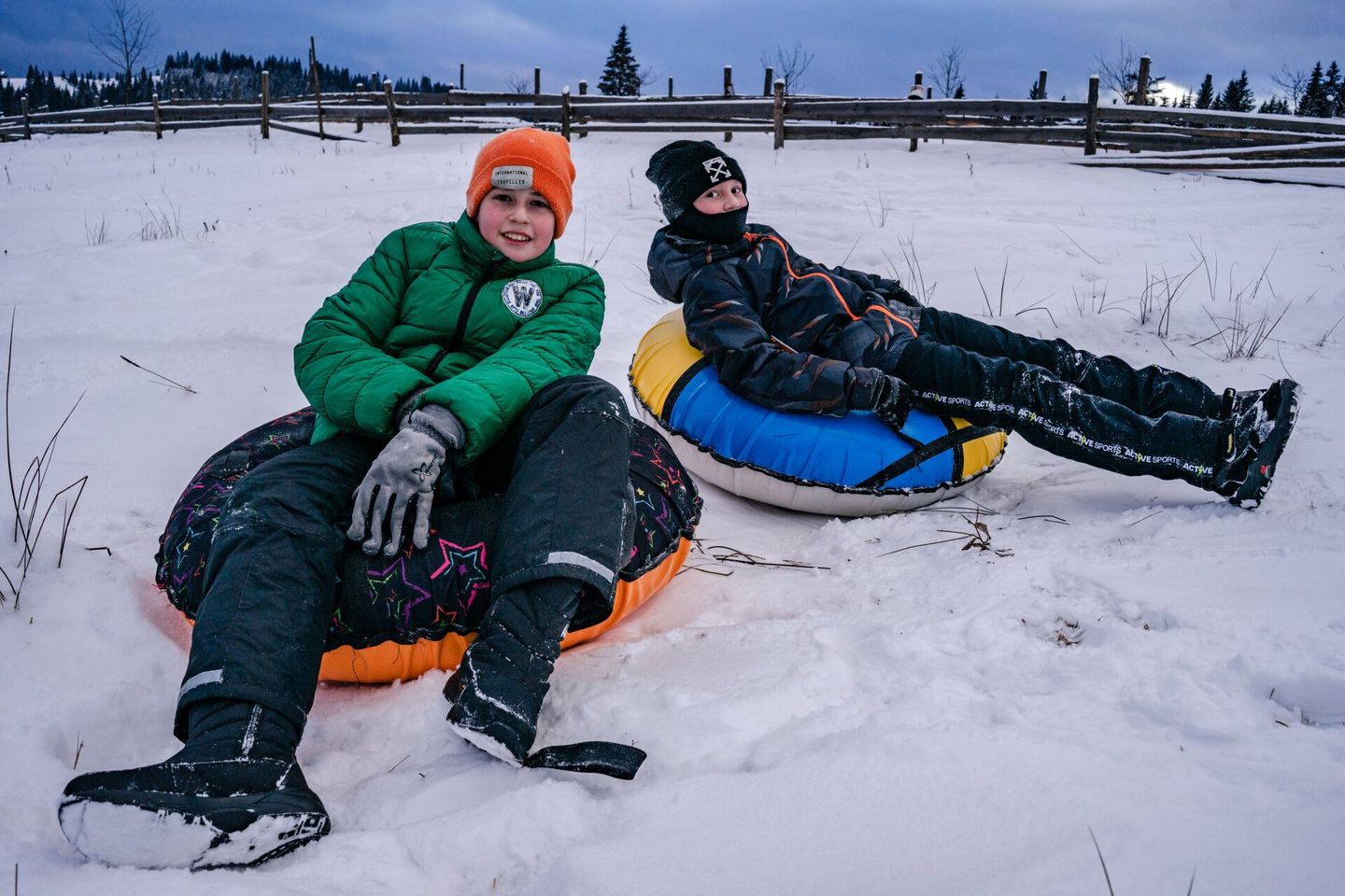 Two children are sitting on snow tubes in the snow.