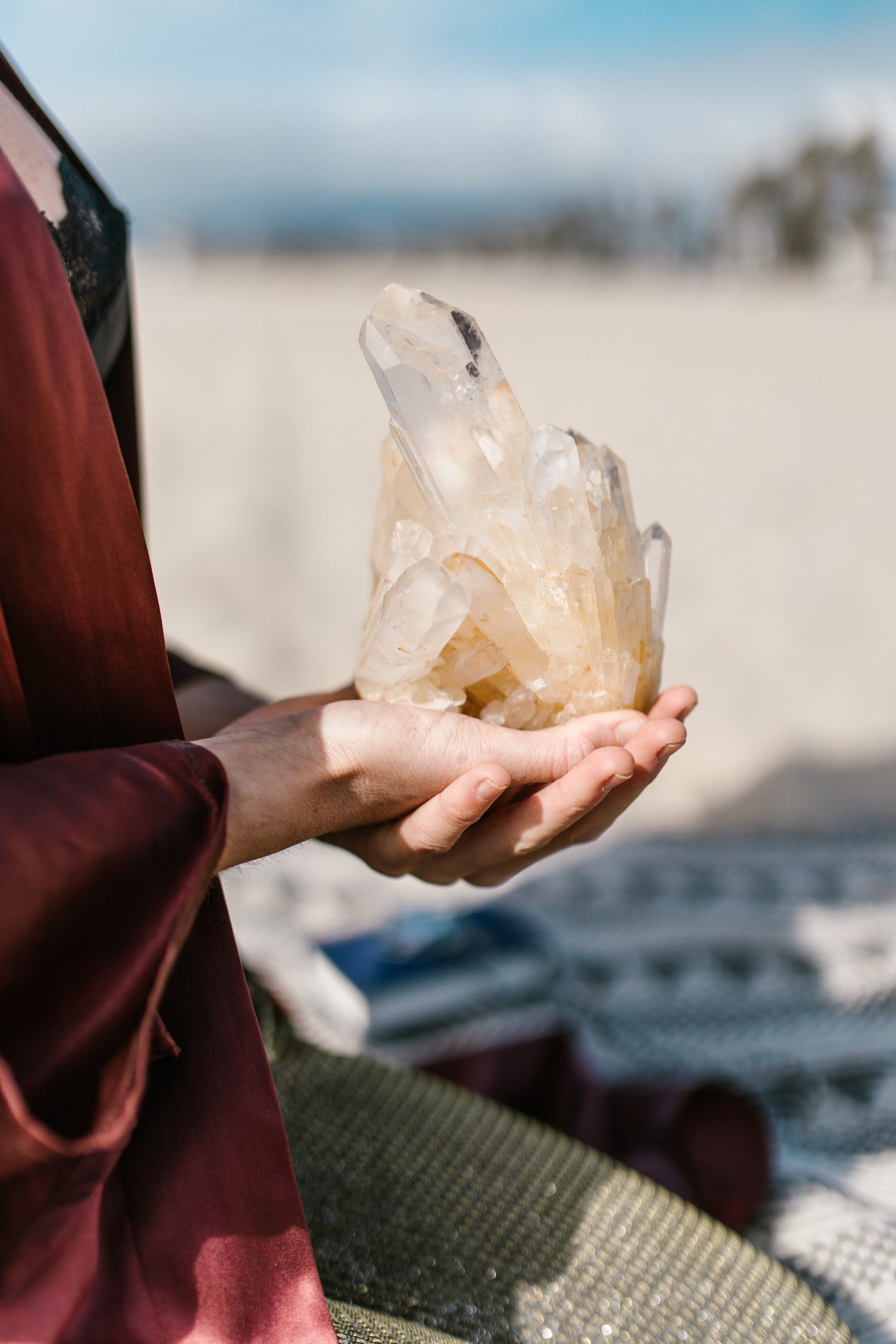 Een persoon die een groot, lichtgekleurd kwartskristal vasthoudt op een zandstrand.