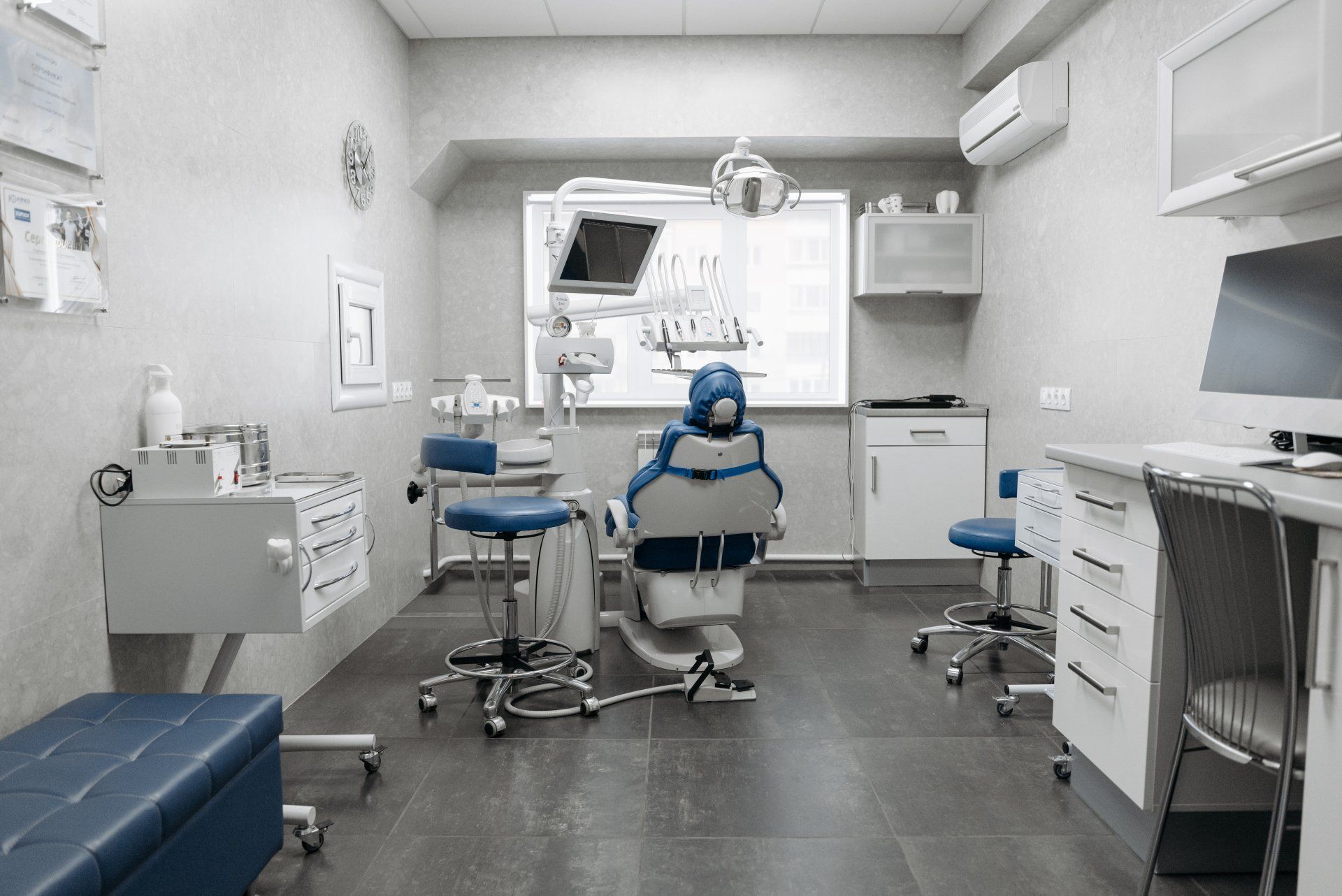 Dental office interior with dental chair, equipment, and cabinets; gray and blue accents.