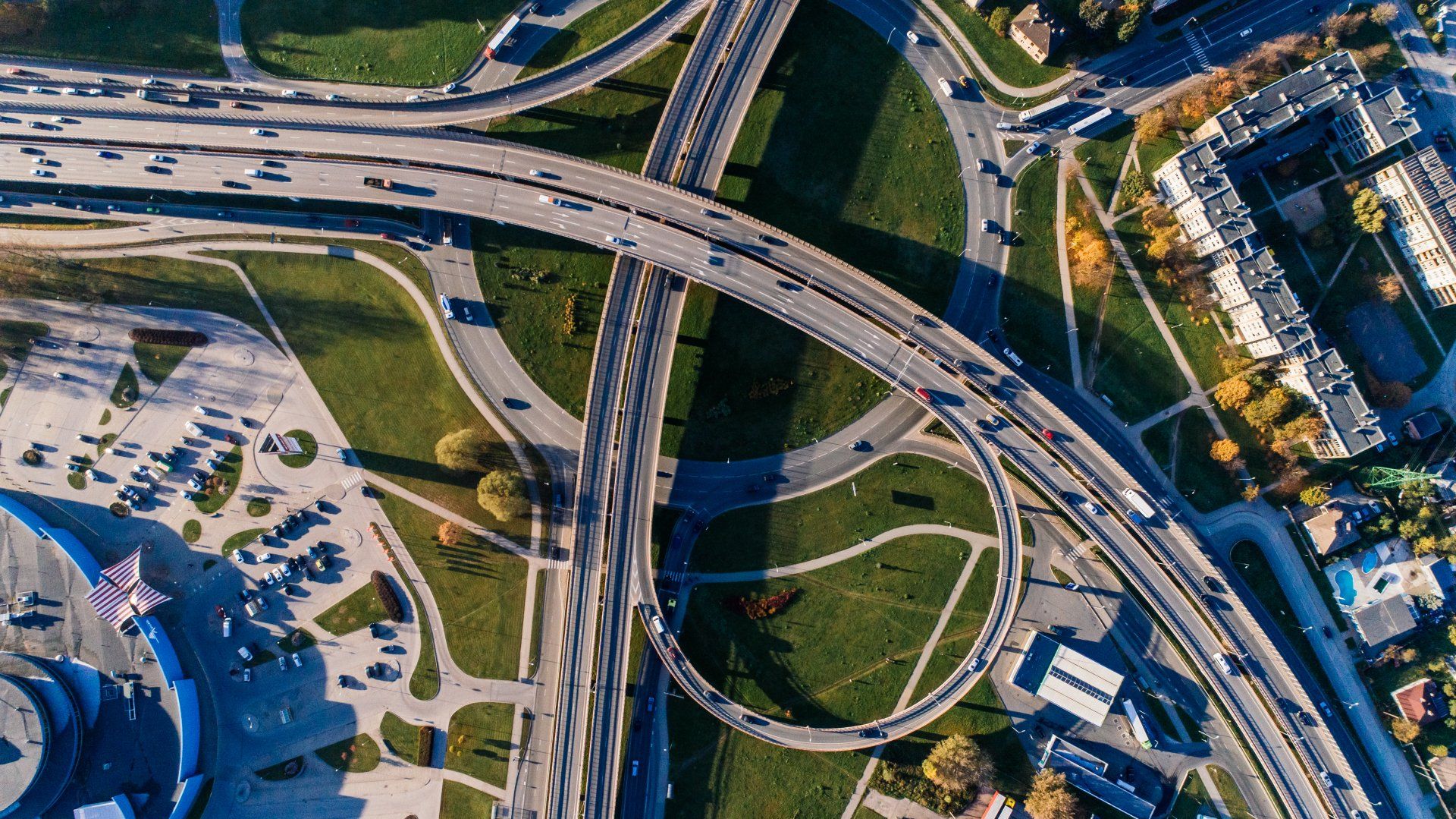 Aerial view of a highway interchange with looping ramps, cars, and surrounding buildings.