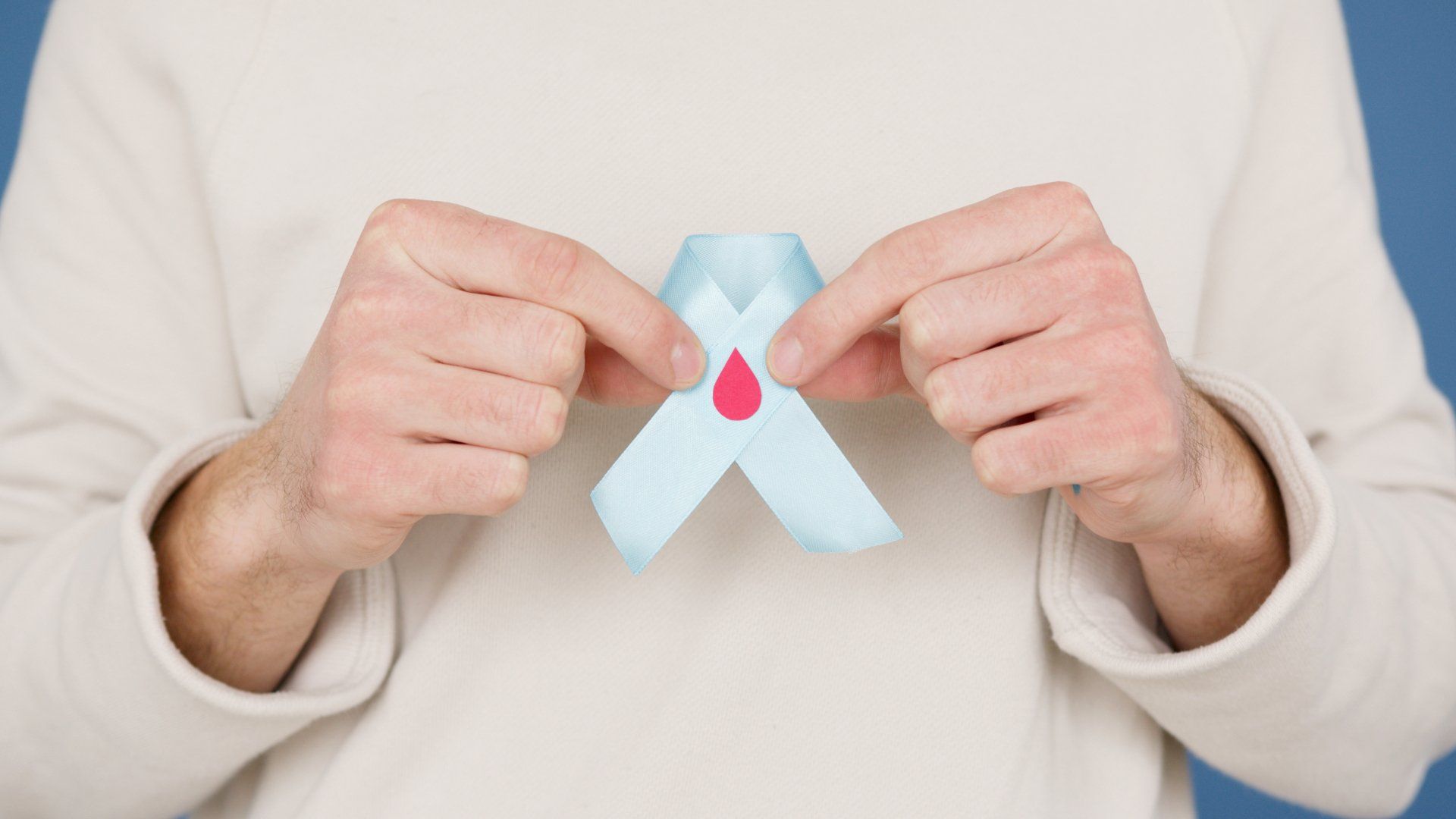 A person is holding a blue ribbon with a red drop on it.