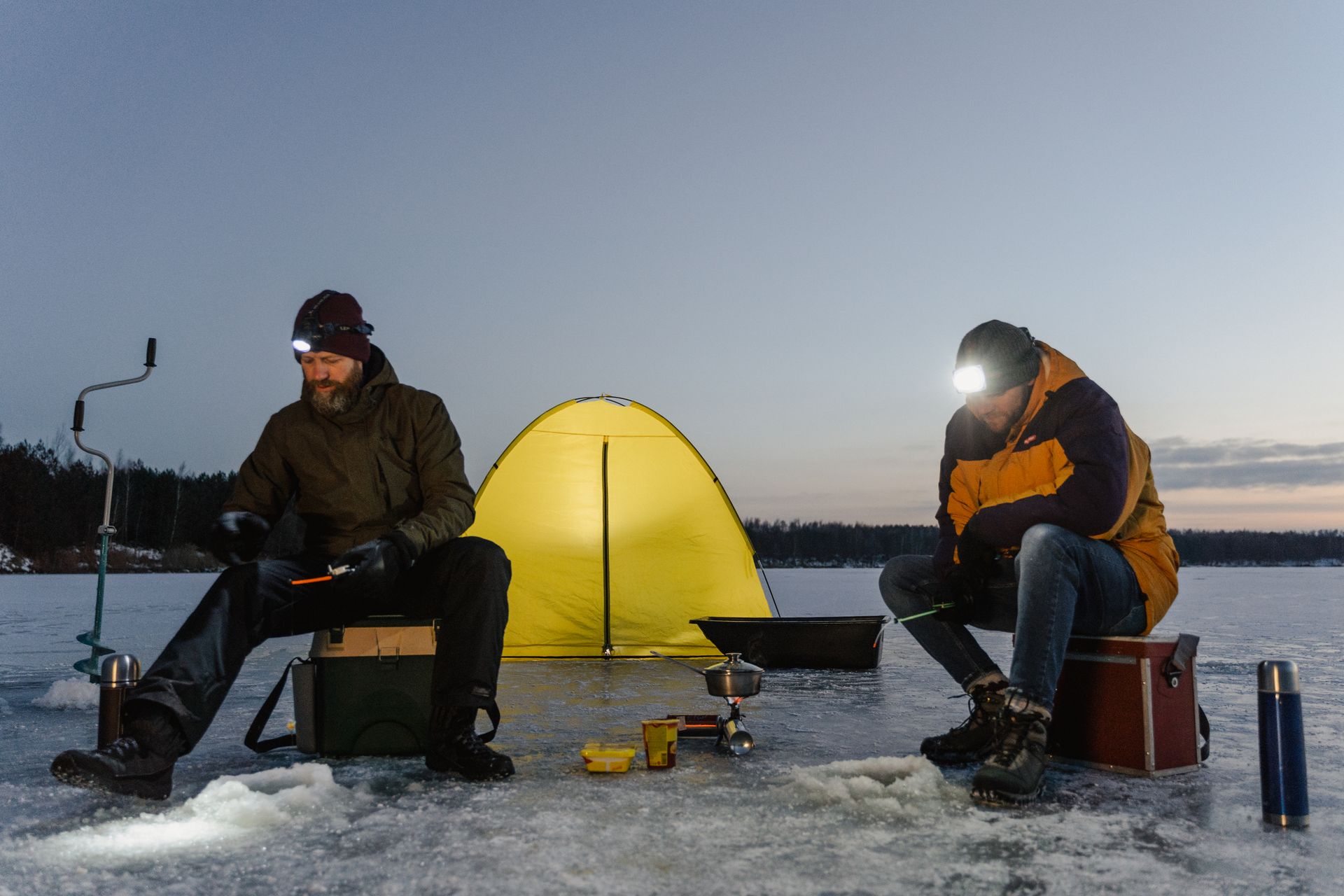 Two men are ice fishing on a lake at night.