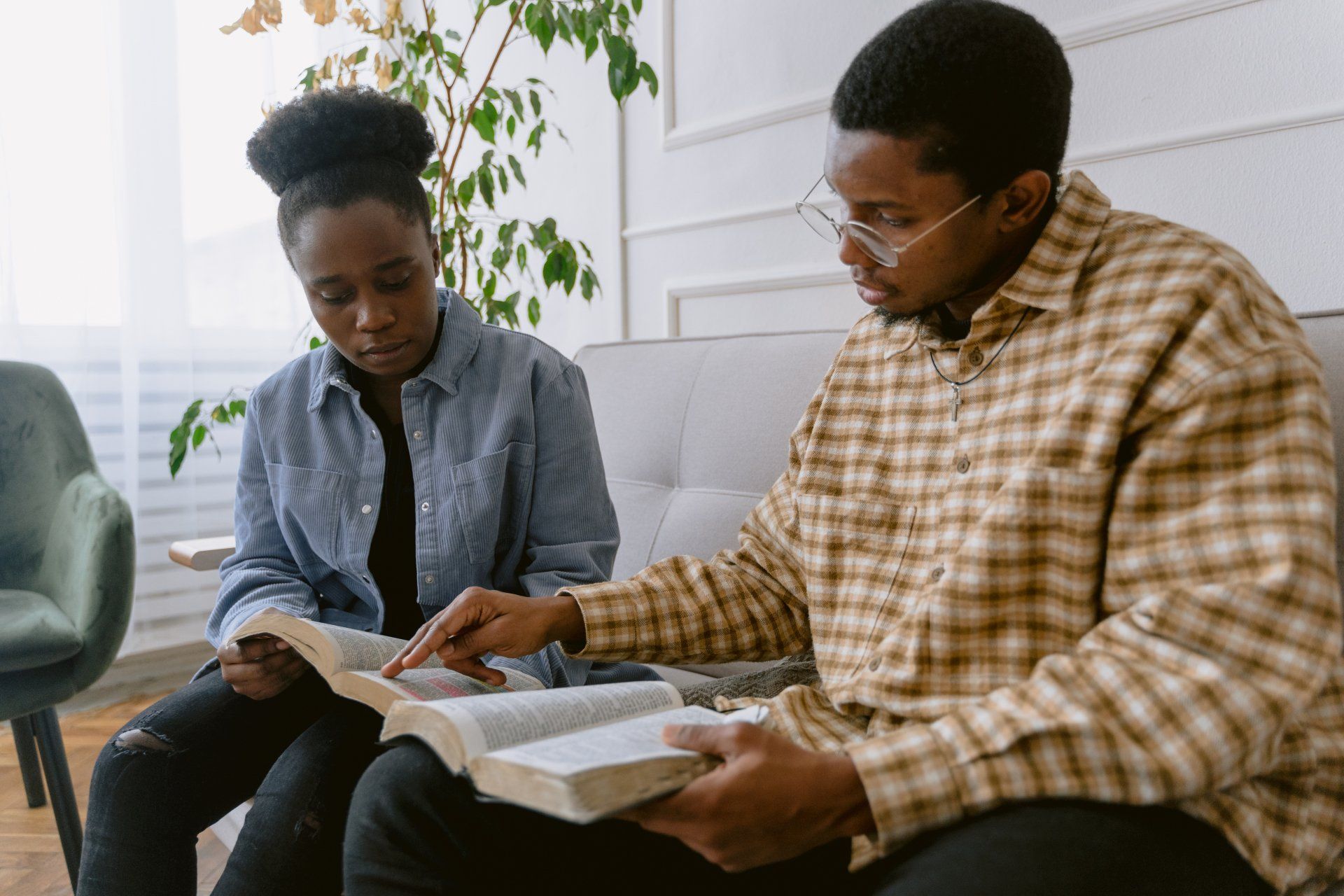 A man and a woman are sitting on a couch reading books.