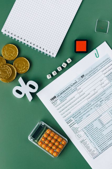 A calculator , coins , a notebook , and a tax form are on a green table.