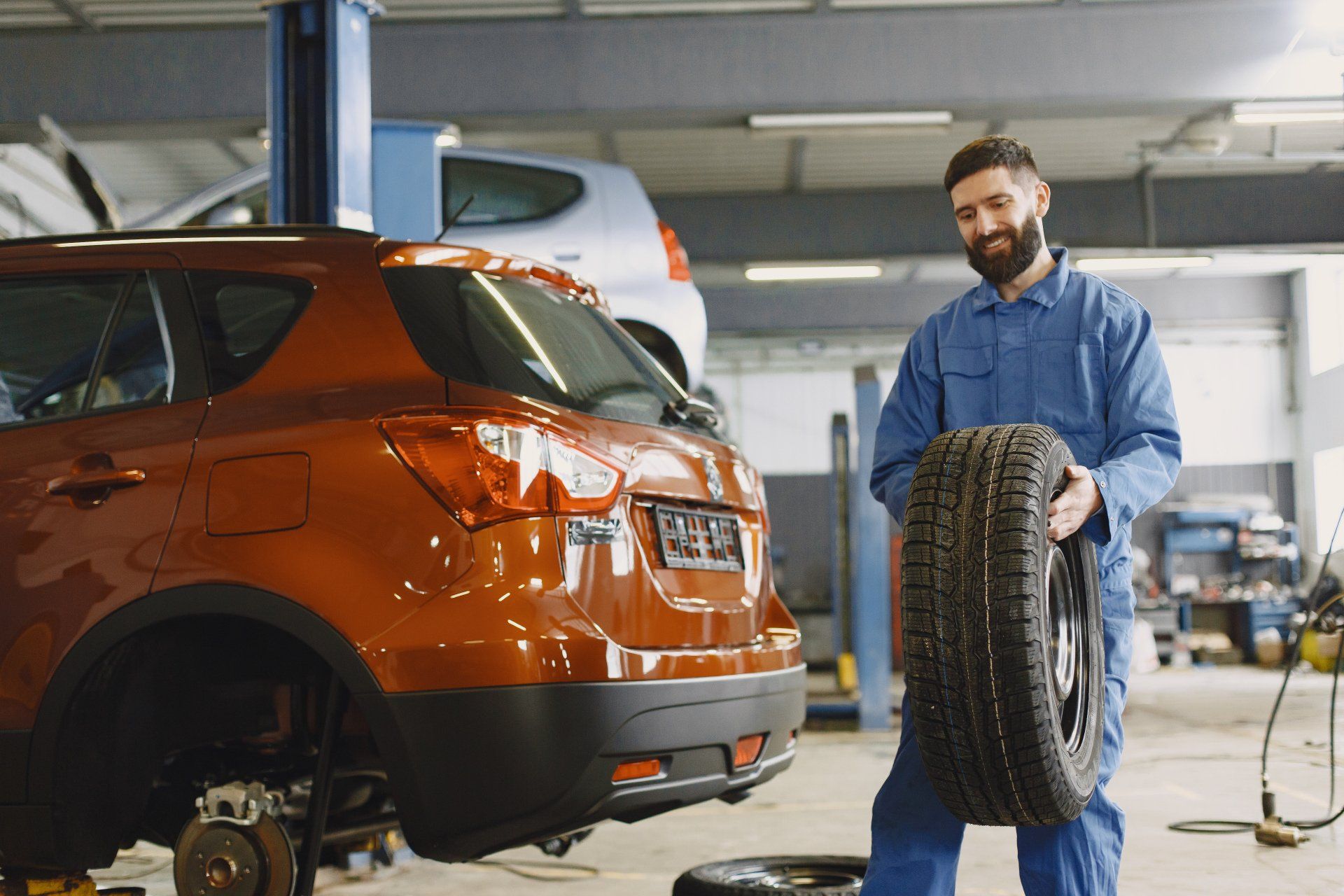 Mechanic Holding A Tire While Inspecting A Vehicle On A Lift In A Service Bay | Kingwood Tire & Automotive