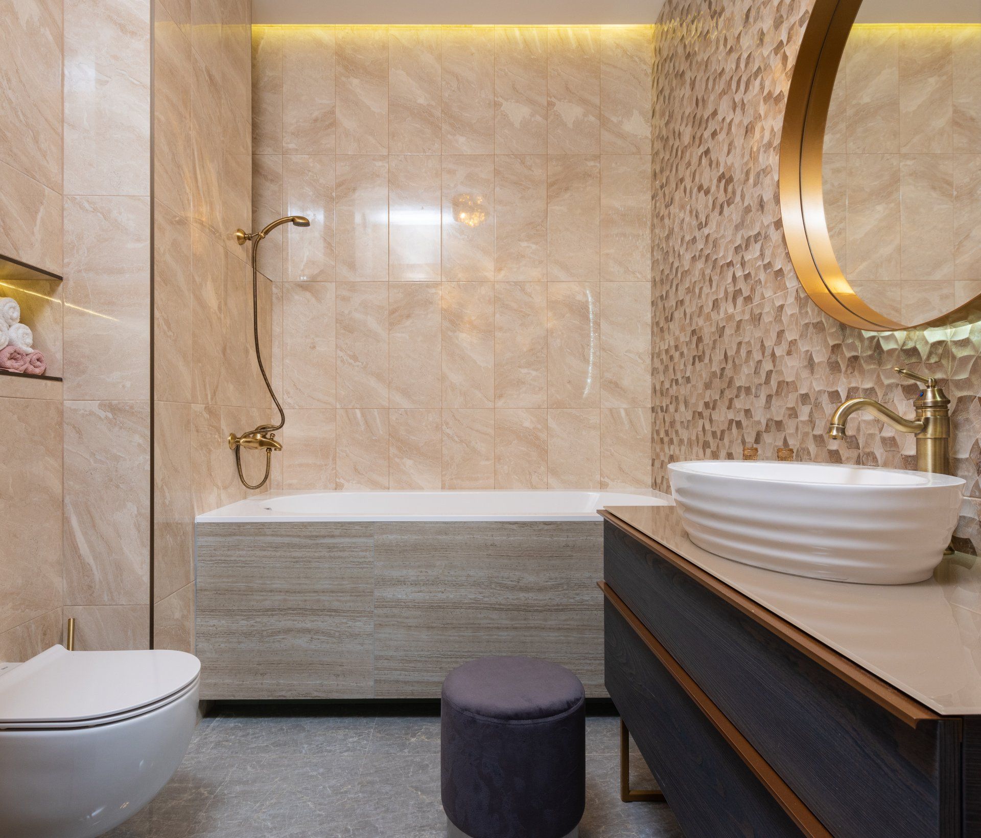 luxury bathroom with a tan tiled shower and a geometric shape tan accent wall with gold fixtures on the shower and the sink.