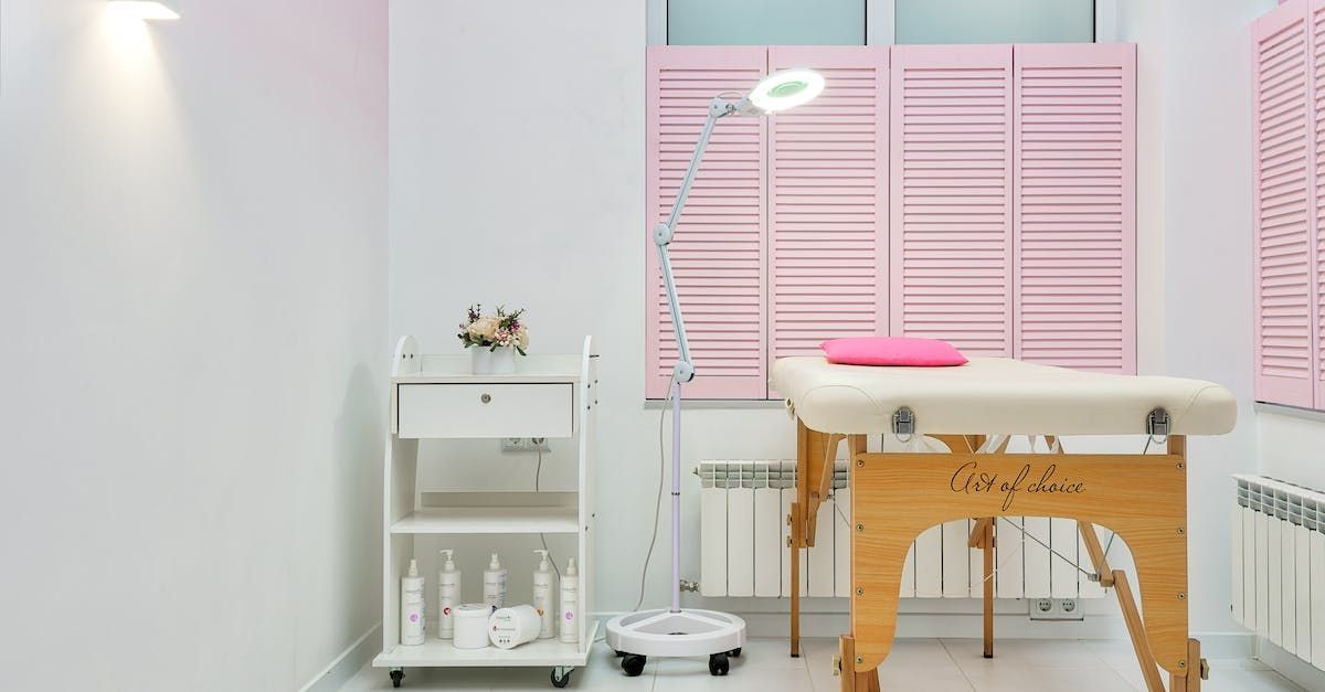 Massage room with pink shutters, treatment table, and a rolling cart with products.