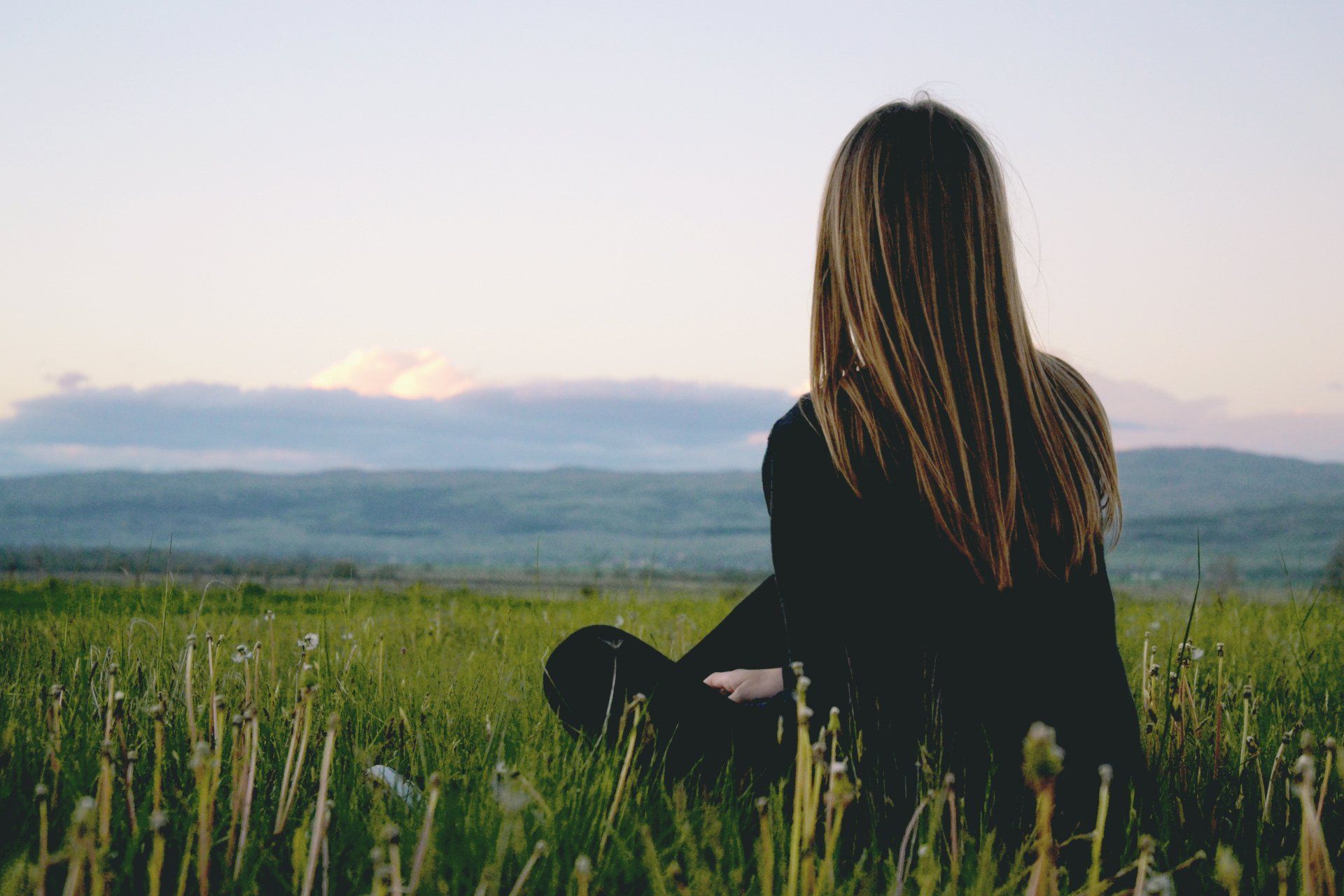 Woman sitting on grass, looking out to countryside and rolling hilss