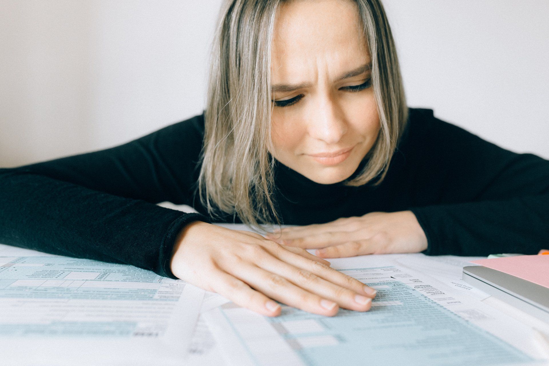 Une femme à l'air inquiet regarde des documents sur un bureau. Elle porte une chemise noire à manches longues dans un environnement bien éclairé.