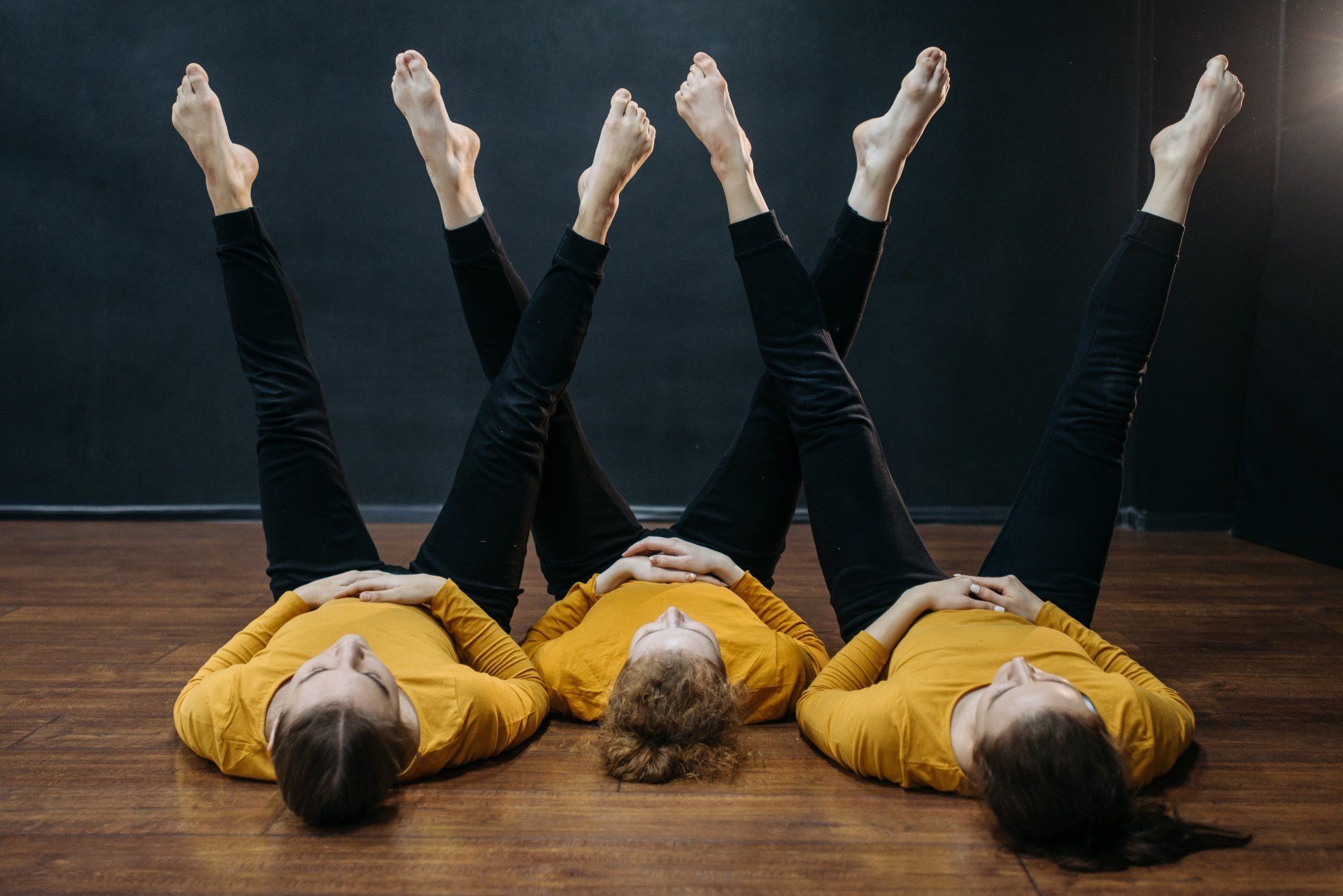Three women are laying on the floor with their legs up in the air.