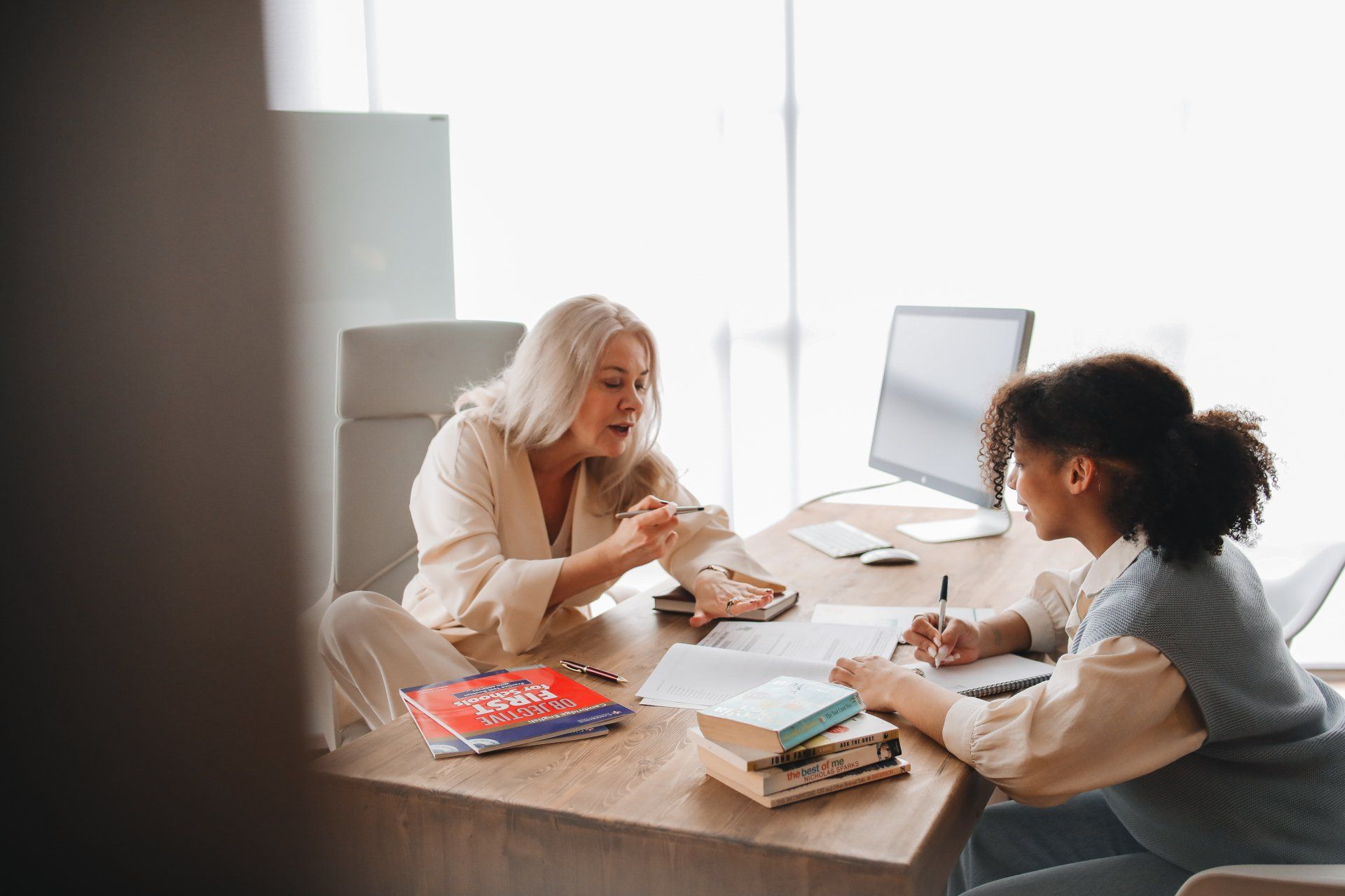 A woman is sitting at a desk talking to another woman.