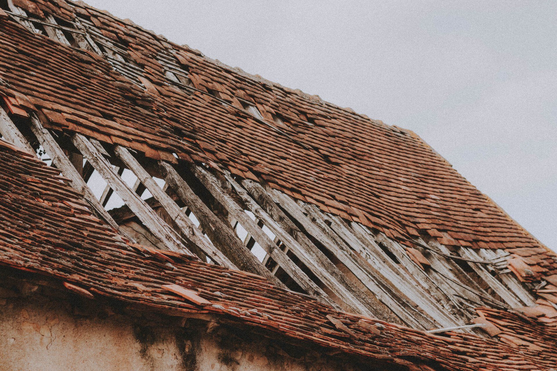 Damaged red tile roof with large sections missing, exposing wooden rafters.