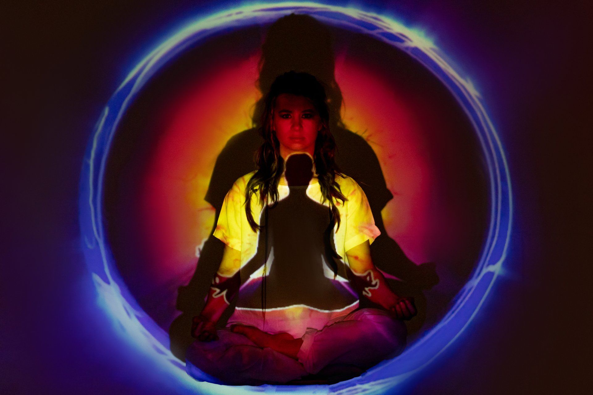 Person meditating in lotus pose, glowing in neon yellow and purple light inside a blue circle.