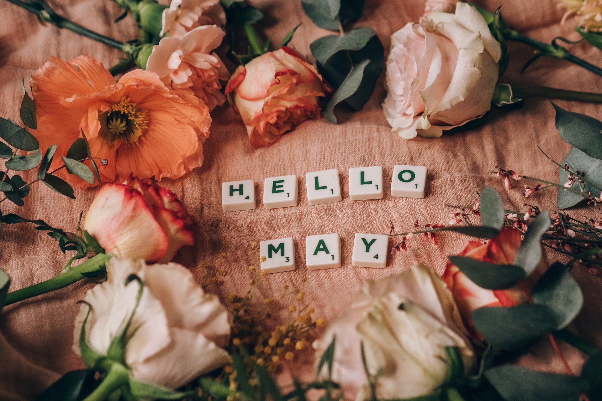 a bunch of flowers are laying on a table with scrabble tiles that say `` hello may '' .