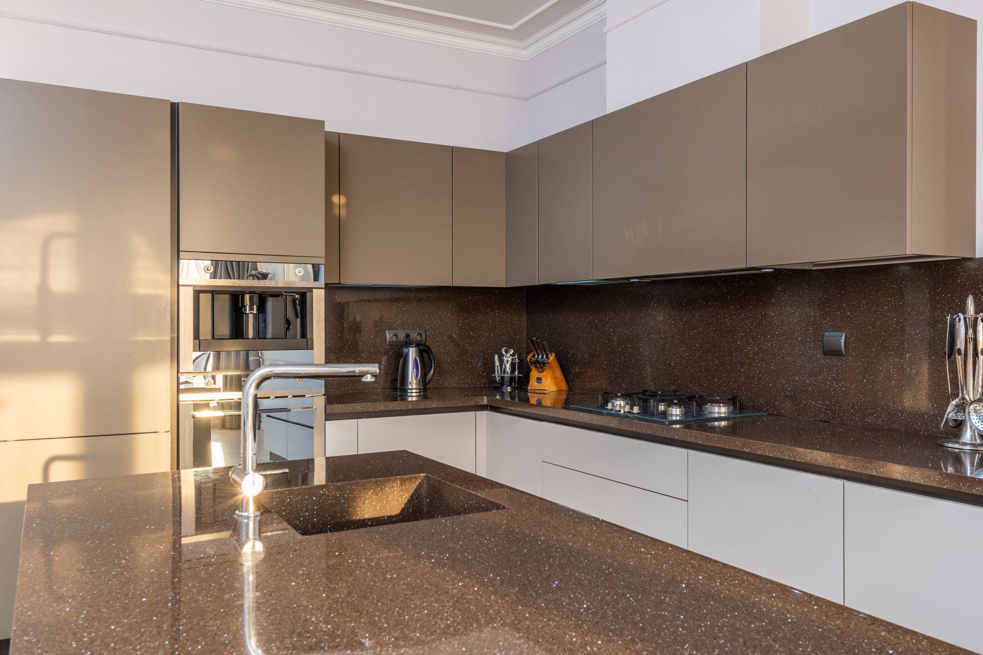 Modern kitchen with brown cabinets, granite counters, and a central sink under bright sunlight