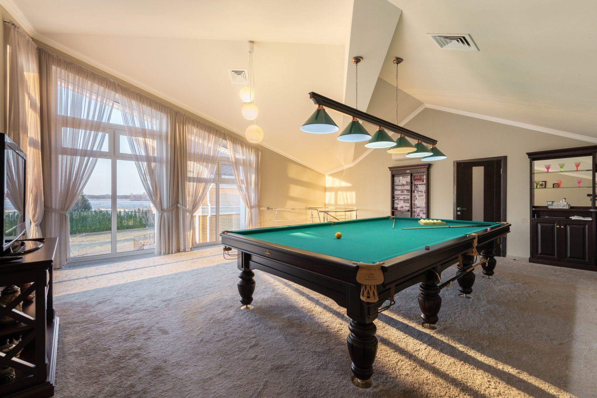 Bright game room with a pool table, large windows, and hanging pendant lights