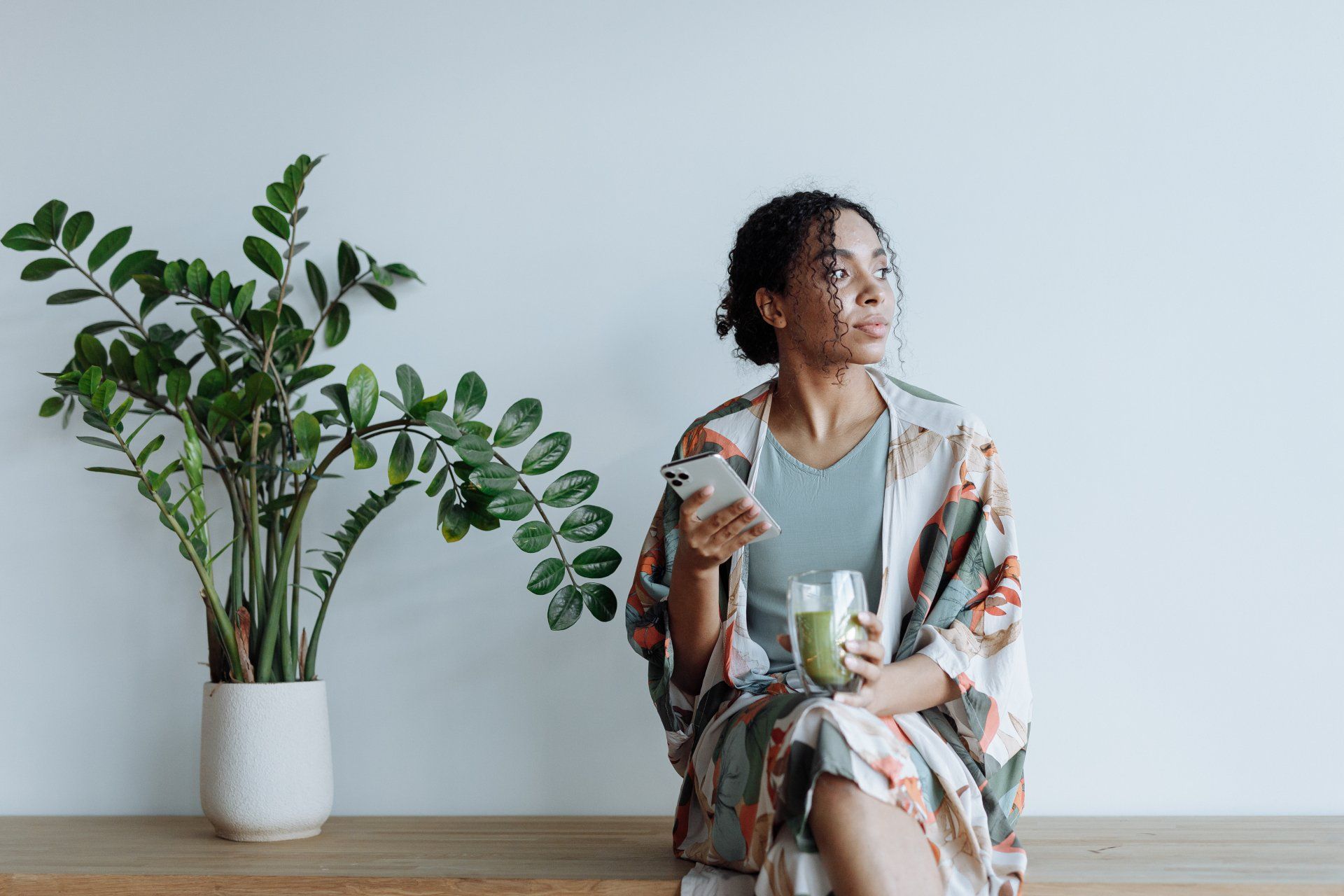 a woman sits on a bench holding a drink and a cell phone