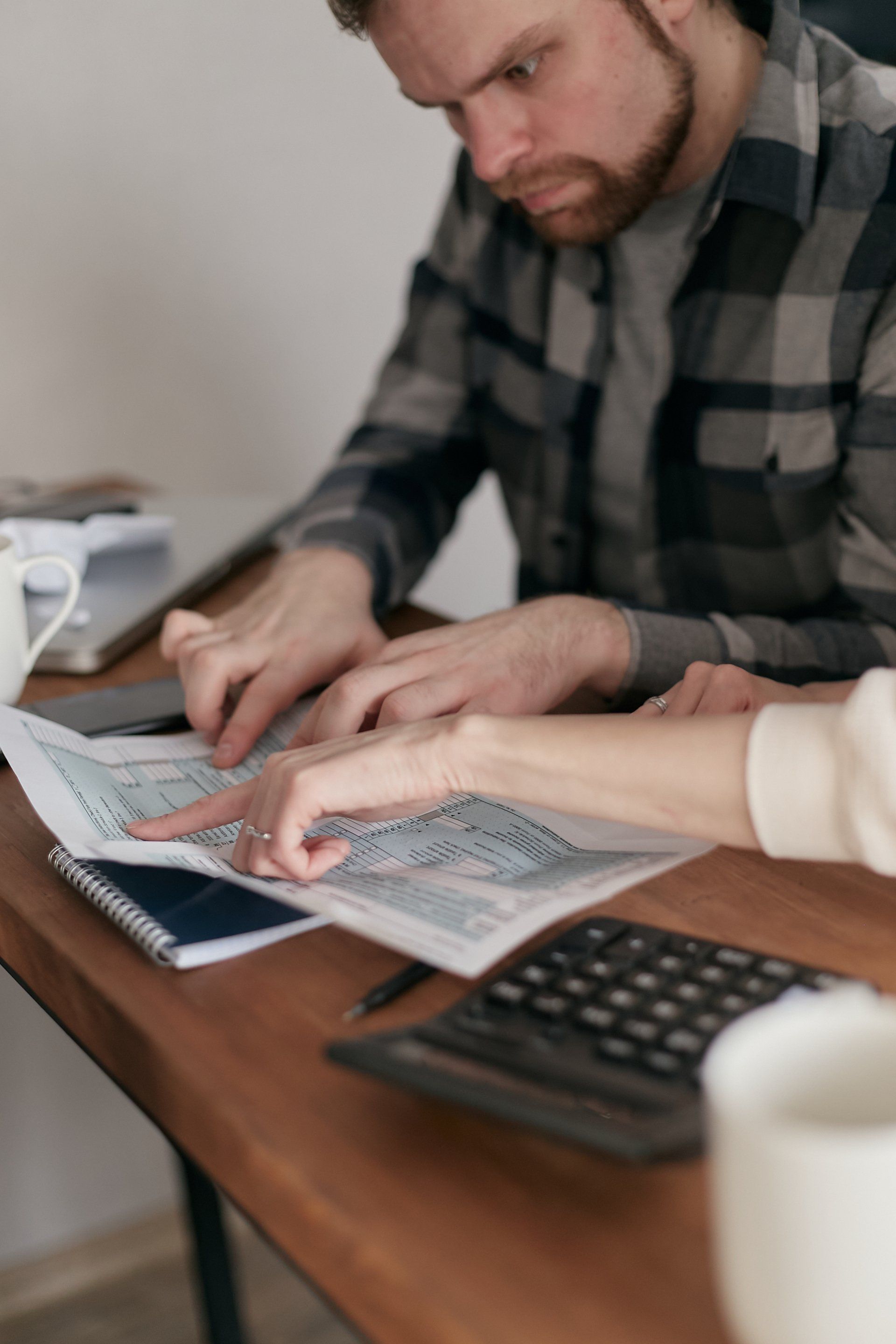 Person pointing at tax form with another person; calculator and notebook on wooden table.