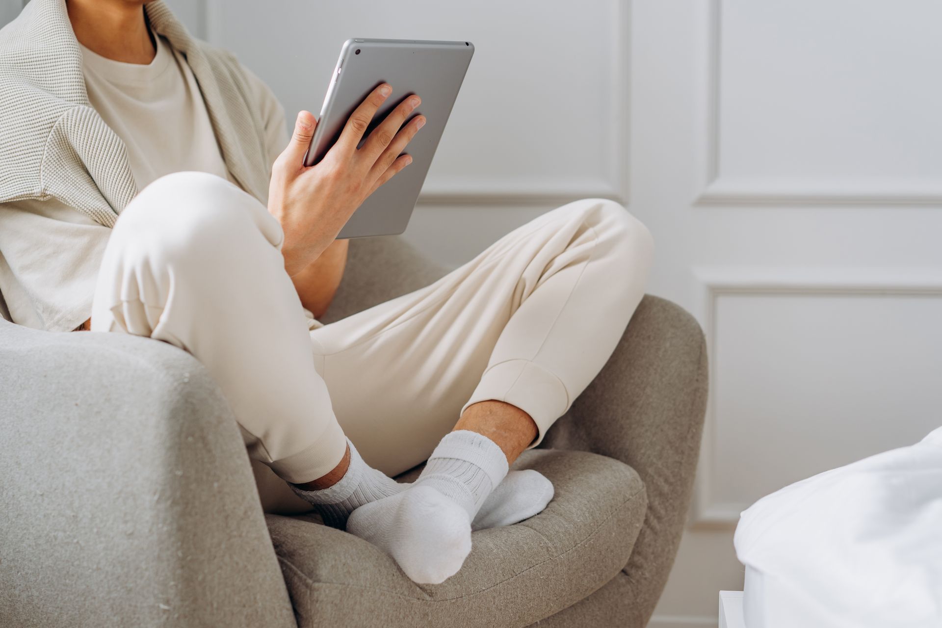 Person seated in a light beige outfit, using a tablet, in a bright, neutral-toned room.